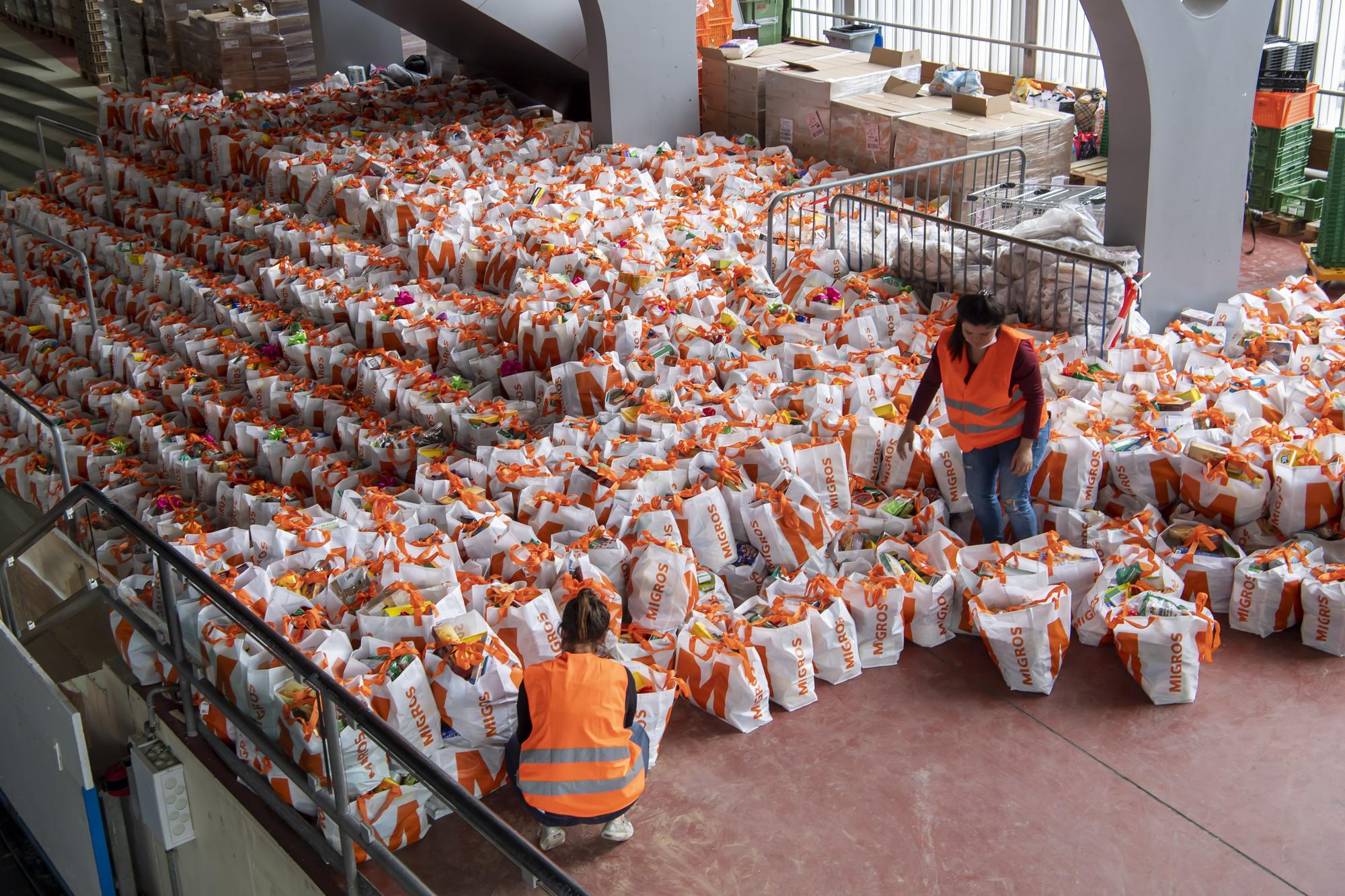 People queue to receive bags with free food and essential products received from donations at the ice stadium Les Vernets, in Geneva, Switzerland, Saturday, May 16, 2020. Following the pandemic coronavirus COVID-19 casts a spotlight on the usually invisible poor people of Geneva. (Martial Trezzini/Keystone via AP)