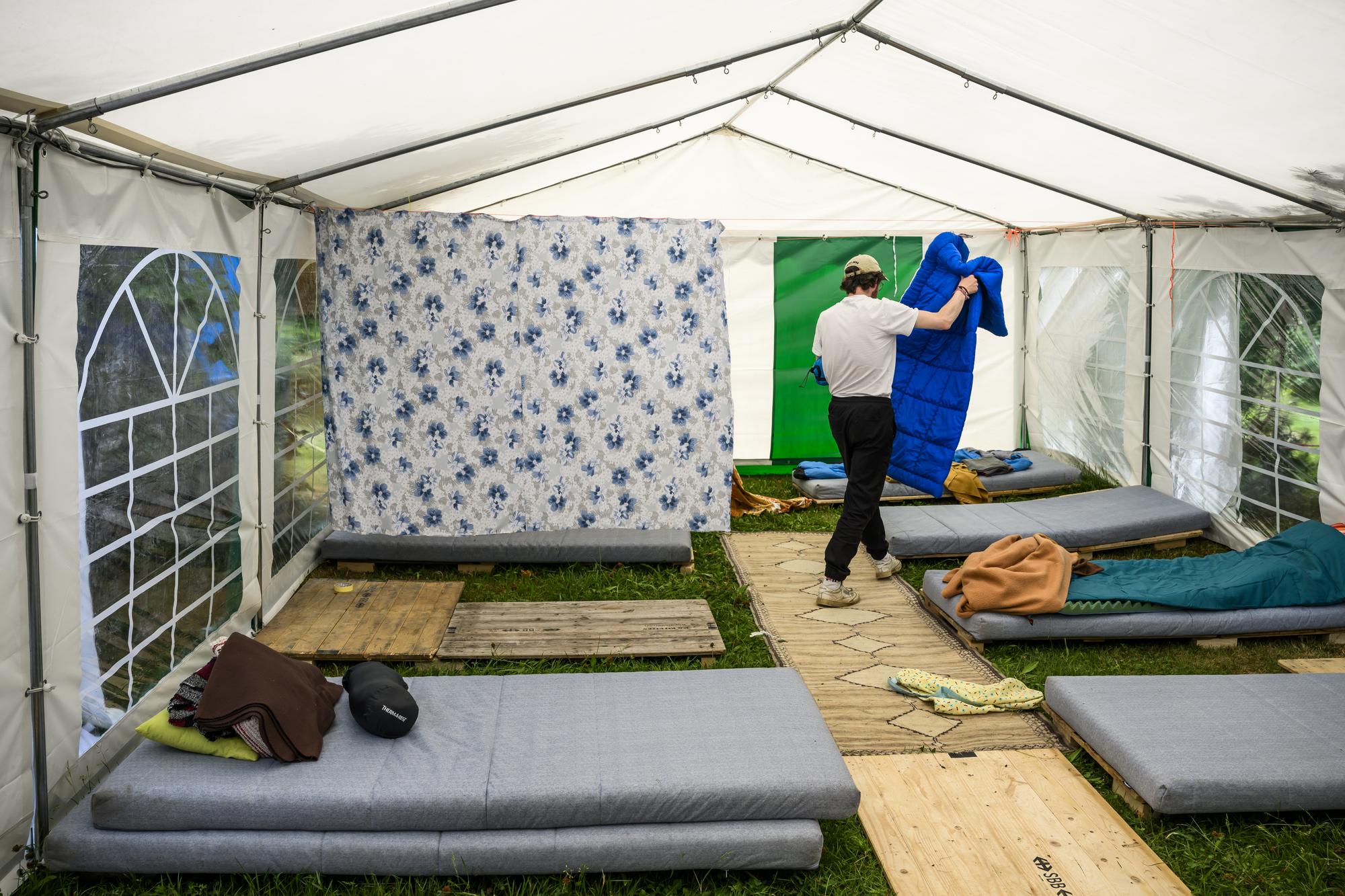 Un militant prepare le dortoir dans l'hebergement d'urgence pour sans-abris installe par le collectif 43m2 dans les jardins de la Haute ecole de travail social de Lausanne (HETSL) le jeudi 2 juin 2022 a Lausanne. (KEYSTONE/Jean-Christophe Bott)