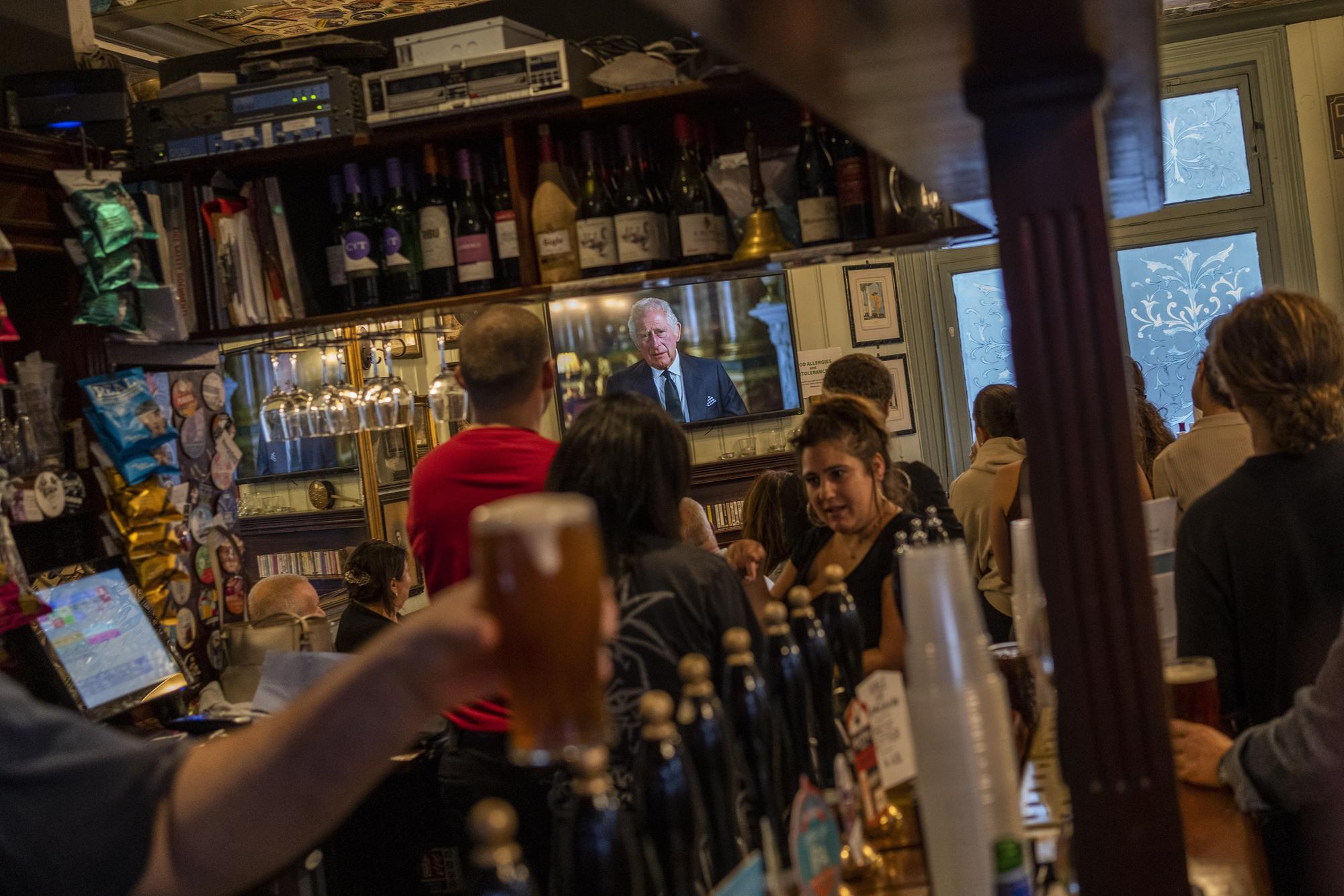 People watch the televised speech of the new King Charles III inside a pub in London, Friday, Sept. 9, 2022. King Charles III says he feels "profound sorrow" over the death of his mother, Queen Elizabeth II, and vows to carry on her "lifelong service" to the nation. Charles is making his first address to the nation as monarch Friday. (AP Photo/Bernat Armangue)