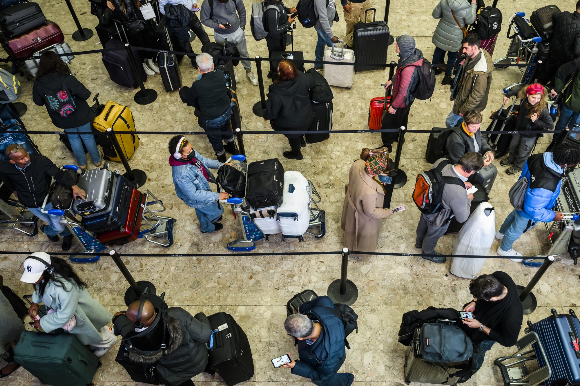 Des voyageurs avec des bagages attendent a l'enregistrement pour faire un voyage en avion avant les fetes le vendredi 23 decembre 2022 a Geneve Aeroport. (KEYSTONE/Jean-Christophe Bott)
