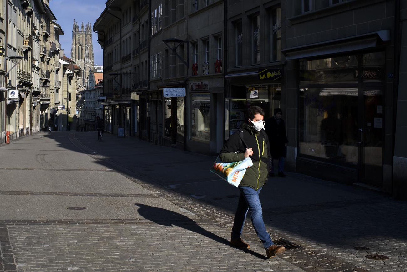 Un homme portant un masque marche dans la rue de Lausanne lors de la pandemie de coronavirus (covid-19), ce mercredi 25 mars 2020, a Fribourg. (KEYSTONE/Anthony Anex)
