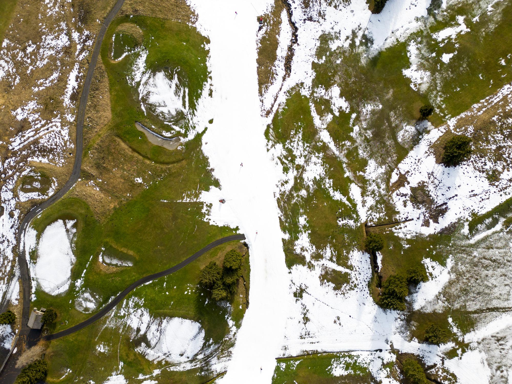 Skiers speed down a ski slope with artificial snow in the middle of a snowless golf course, at 1600 meters above sea level, in the alpine resort of Villars-sur-Ollon, Switzerland, Saturday, December 31, 2022. The mild weather of the last few days in the Swiss Alps has disrupted the activity of alpine ski resorts below an altitude of 2200 meters above sea level. (KEYSTONE/Laurent Gillieron)