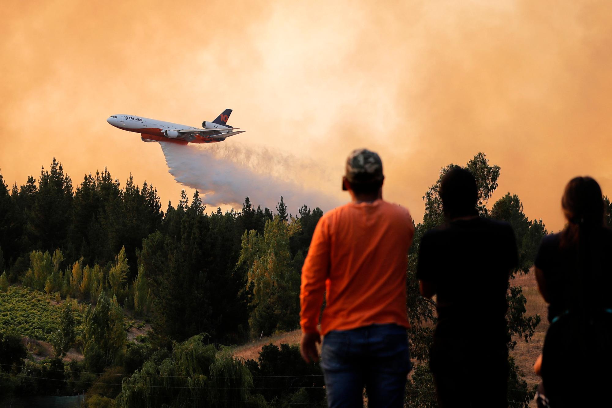 A local takes snapshots as a 10 Tanker DC-10 fire plane throws water over a forest fire in Quirihue, Ñuble Region, in Chile, on February 10, 2023. - Forest fires have raged for more than a week in south-central Chile, leaving at least 24 people dead. (Photo by JAVIER TORRES / AFP)