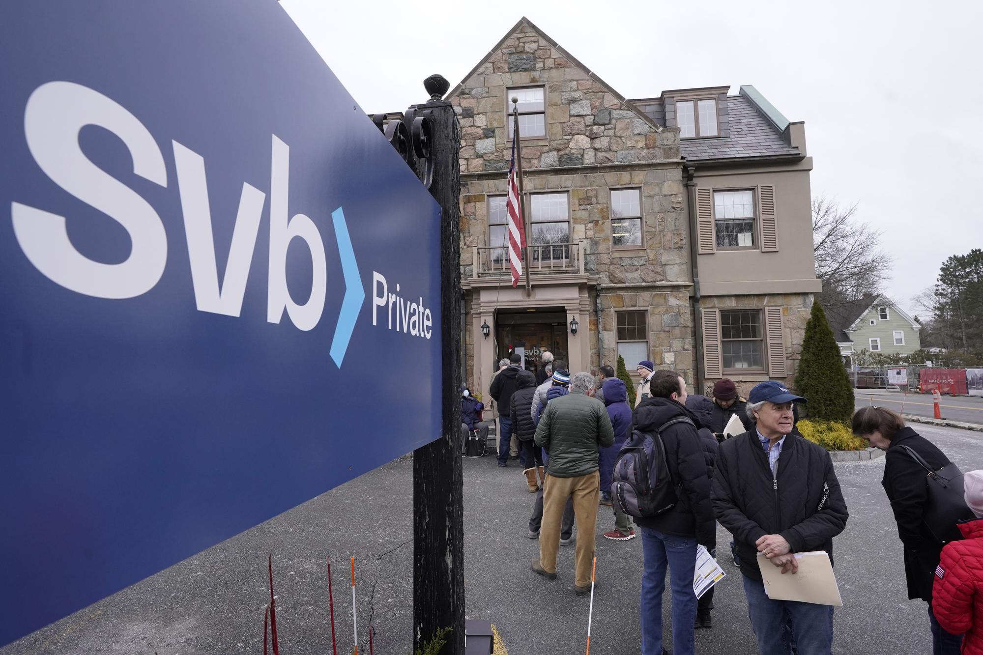 FILE - Customers and bystanders form a line outside a Silicon Valley Bank branch location, Monday, March 13, 2023, in Wellesley, Mass. On March 10, Silicon Valley Bank failed after making a bad bet on falling rates and absorbing big losses in the bond market ? news of which started a massive bank run. (AP Photo/Steven Senne, File)