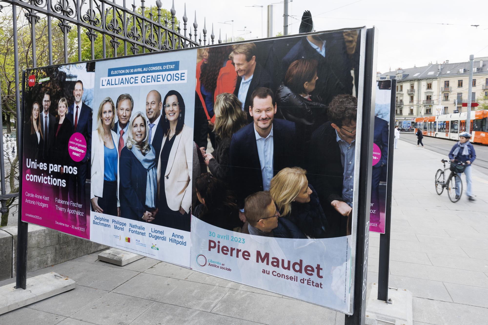 Une personnes passe vers l'affiche electorale du parti Socialiste - Les Verts Carole-Anne Kast / Antonio Hodgers / Fabienne Fischer / Thierry Apotheloz, l'affiche de l'alliance genevoise Delphine Bachmann - UDC / Philippe Morel - MCG / Nathalie Fontanet - PLR / Lionel Dugerdil - UDC / Anne Hiltpold - PLR et l'affiche de Libertes et Justice sociale Pierre Maudet, ce lundi 17 avril 2023 a Geneve. Les citoyens genevois voteront pour l'election du deuxieme tour de l'election du Conseil d'Etat du dimanche 30 avril 2023 (KEYSTONE/Salvatore Di Nolfi)