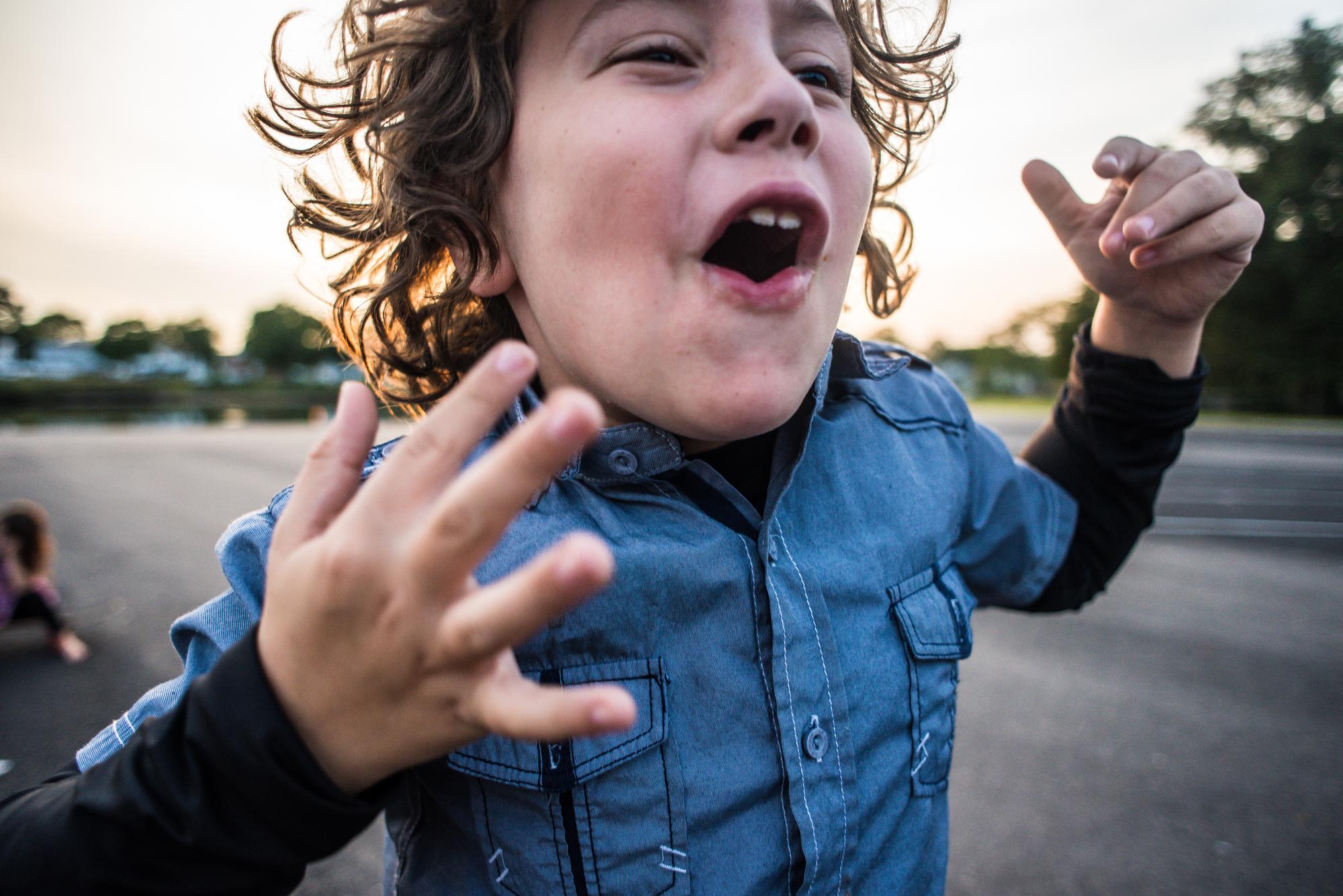 A portrait of a school age boy with curly hair cheering.