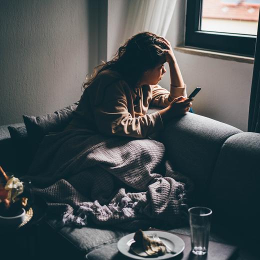 Sad and depressed woman using smartphone at home.