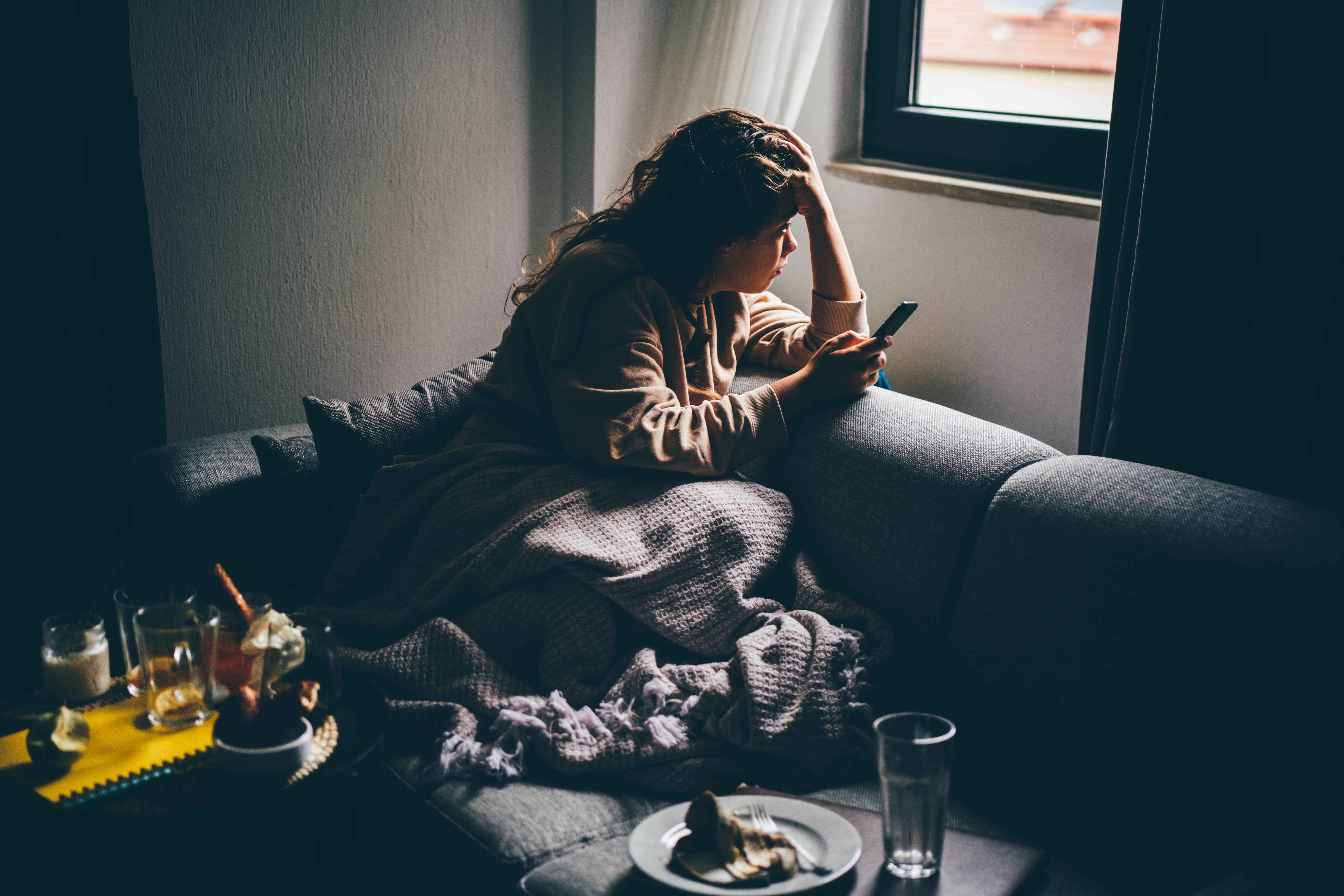 Sad and depressed woman using smartphone at home.