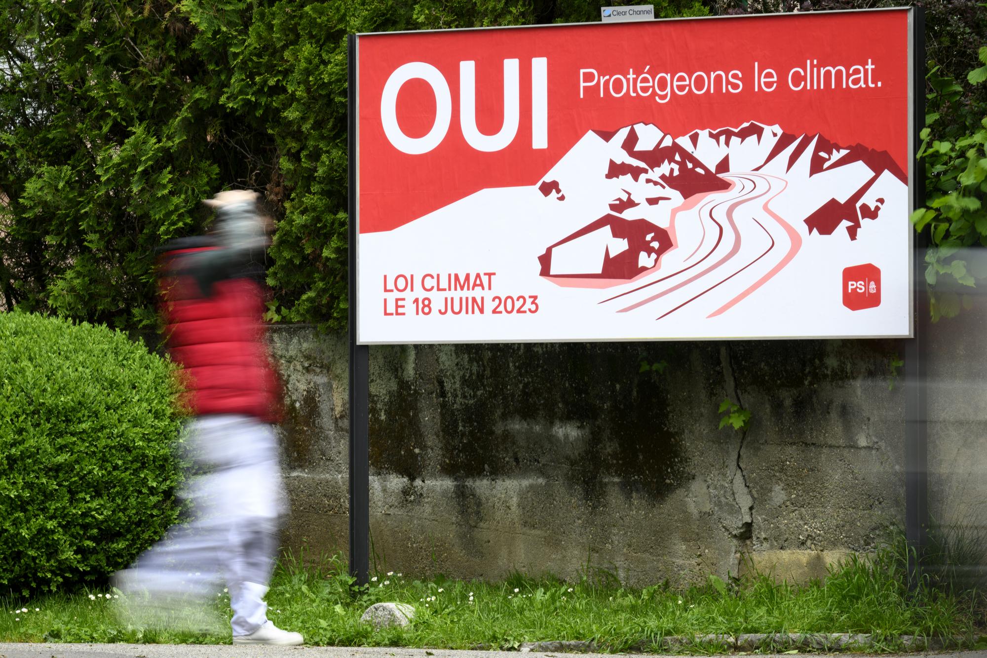 Une personne passe devant une affiche du Parti Socialiste, PS, invitant a voter oui pour la loi sur le climat ce mardi 16 mai 2023 a Lausanne. Le 18 juin prochain la population suisse va se prononcer lors d'une votation populaire sur la loi federale sur les objectifs en matiere de protection du climat, sur l'innovation et sur le renforcement de la securite energtique (LCI). (KEYSTONE/Laurent Gillieron)