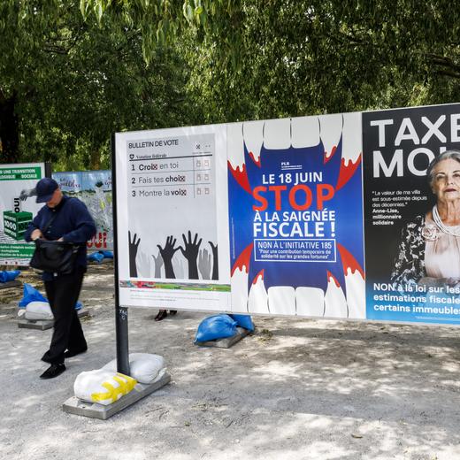 Une personne passe entre les affiches des partis politiques et des associations donnant leurs mots d'ordre pour les votations federales, cantonales et communales du 18 juin, ce dimanche 4 juin 2023 a Geneve. Les citoyens suisses et genevois se prononceront sur trois objets federaux: Arrete federal sur une imposition particuliere des grands groupes d'entreprises, Loi sur les objectifs en matiere de protection du climat et sur la Loi federale COVID-19 et des 6 objets cantonaux genevois. (KEYSTONE/Salvatore Di Nolfi)