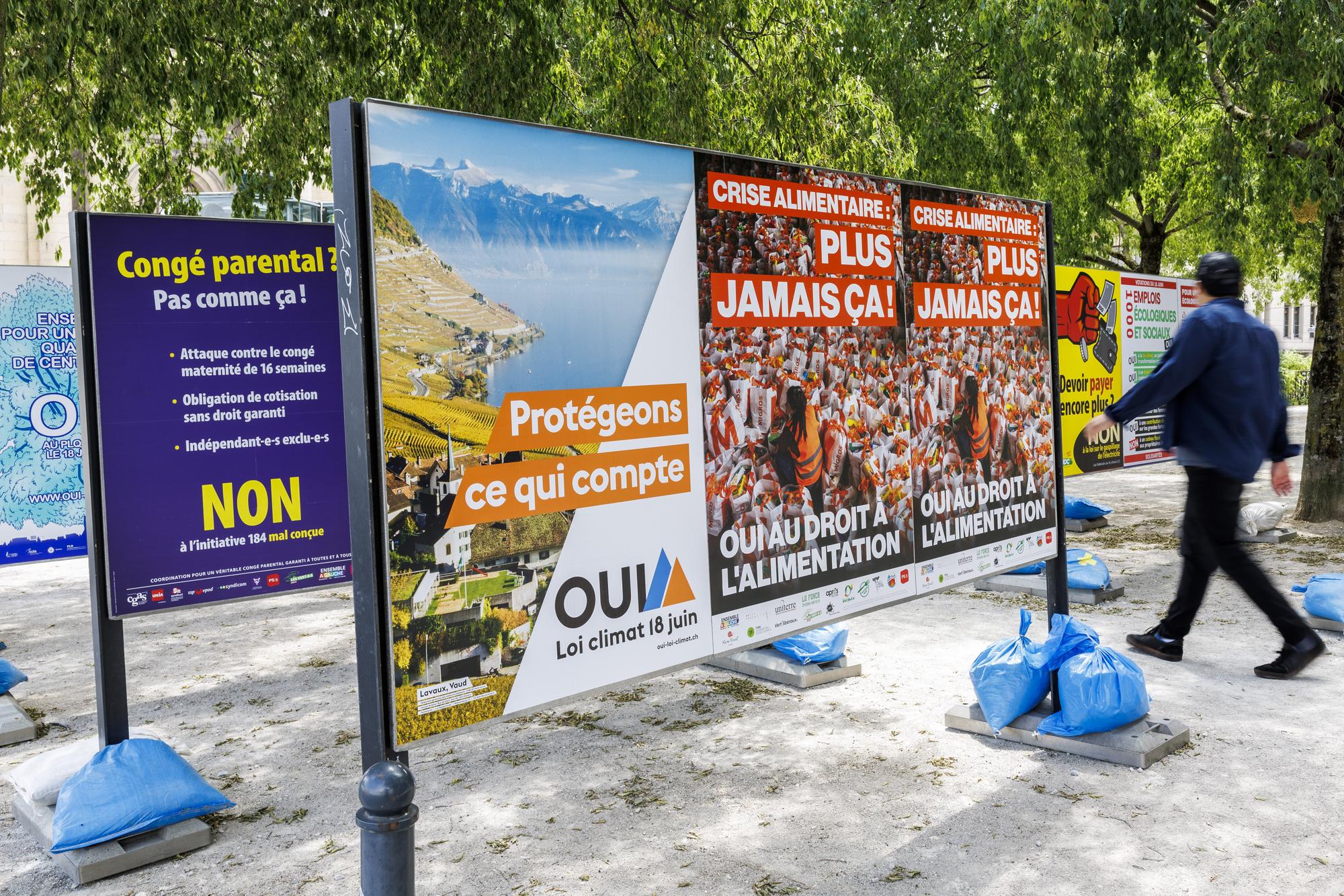 Une personne passe vers les affiches des partis politiques et des associations donnant leurs mots d'ordre pour les votations federales, cantonales et communales du 18 juin, ce dimanche 4 juin 2023 a Geneve. Les citoyens suisses et genevois se prononceront sur trois objets federaux: Arrete federal sur une imposition particuliere des grands groupes d'entreprises, Loi sur les objectifs en matiere de protection du climat et sur la Loi federale COVID-19 et des 6 objets cantonaux genevois. (KEYSTONE/Salvatore Di Nolfi)