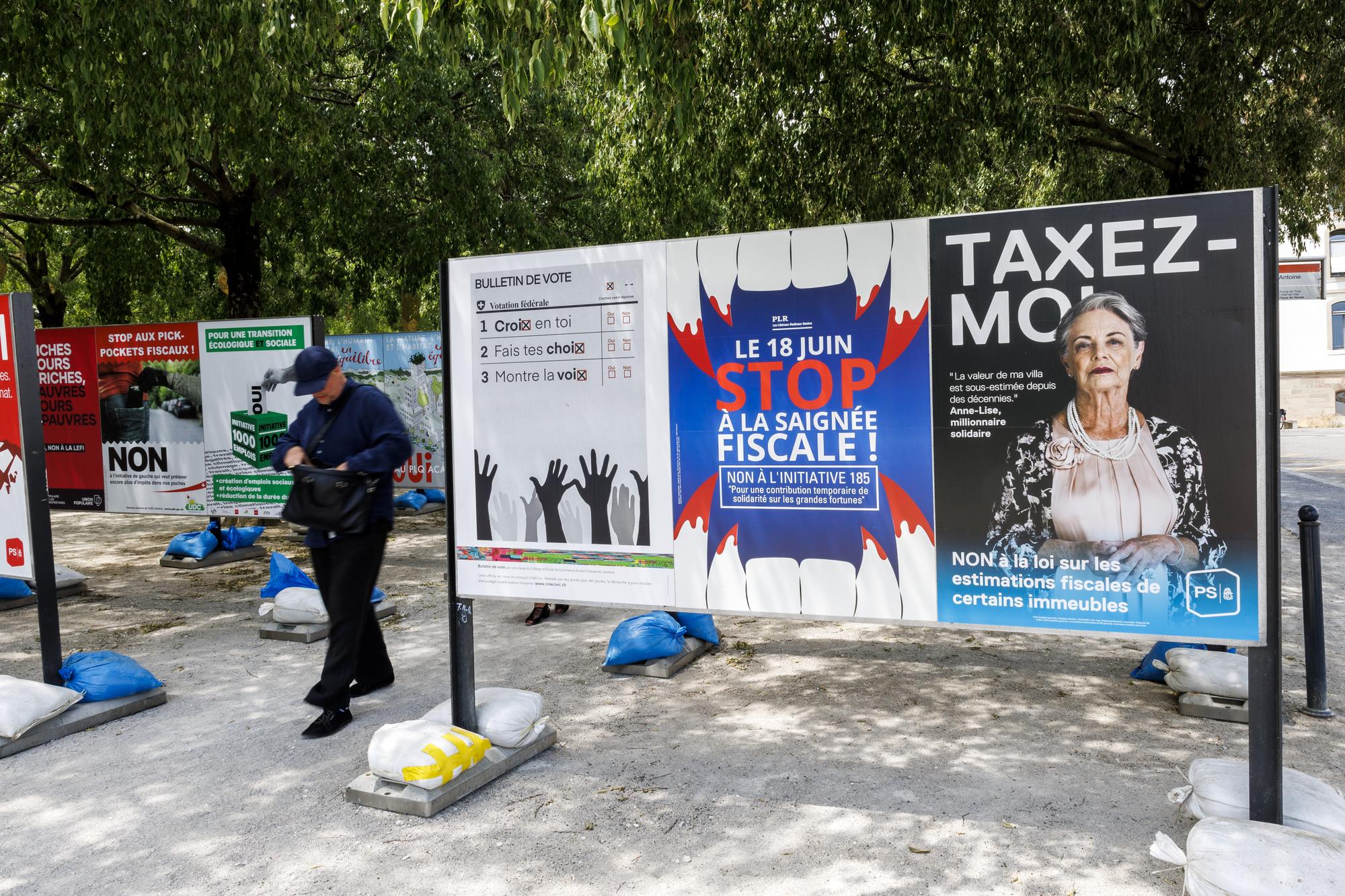Une personne passe entre les affiches des partis politiques et des associations donnant leurs mots d'ordre pour les votations federales, cantonales et communales du 18 juin, ce dimanche 4 juin 2023 a Geneve. Les citoyens suisses et genevois se prononceront sur trois objets federaux: Arrete federal sur une imposition particuliere des grands groupes d'entreprises, Loi sur les objectifs en matiere de protection du climat et sur la Loi federale COVID-19 et des 6 objets cantonaux genevois. (KEYSTONE/Salvatore Di Nolfi)