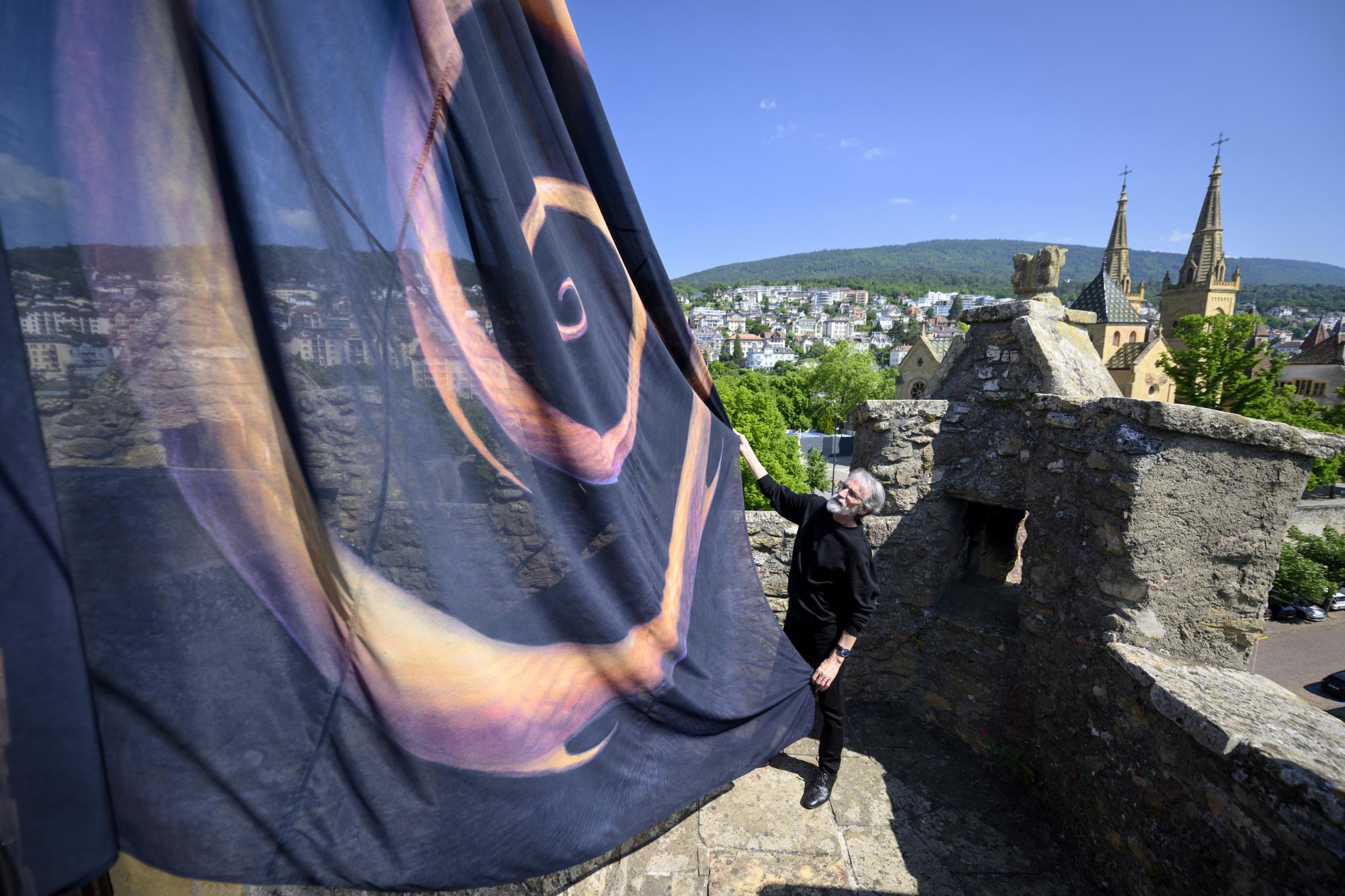 John Howe, artiste et illustrateur hisse un drapeau avec une de ses oeuvre sur le toit de la Tour des prisons et devant la collegiale protestante Notre-Dame de Neuchatel, droite, lors de la presentation a la presse par Le Canton et la Ville de Neuchatel, le Neuchatel International Fantastic Film Festival, NIFFF, et John Howe sur la craation d'un espace dedie au fantastique, a l'art et a l'innovation ce lundi 5 juin 2023 a la Tour des prisons a Neuchatel. (KEYSTONE/Laurent Gillieron)
