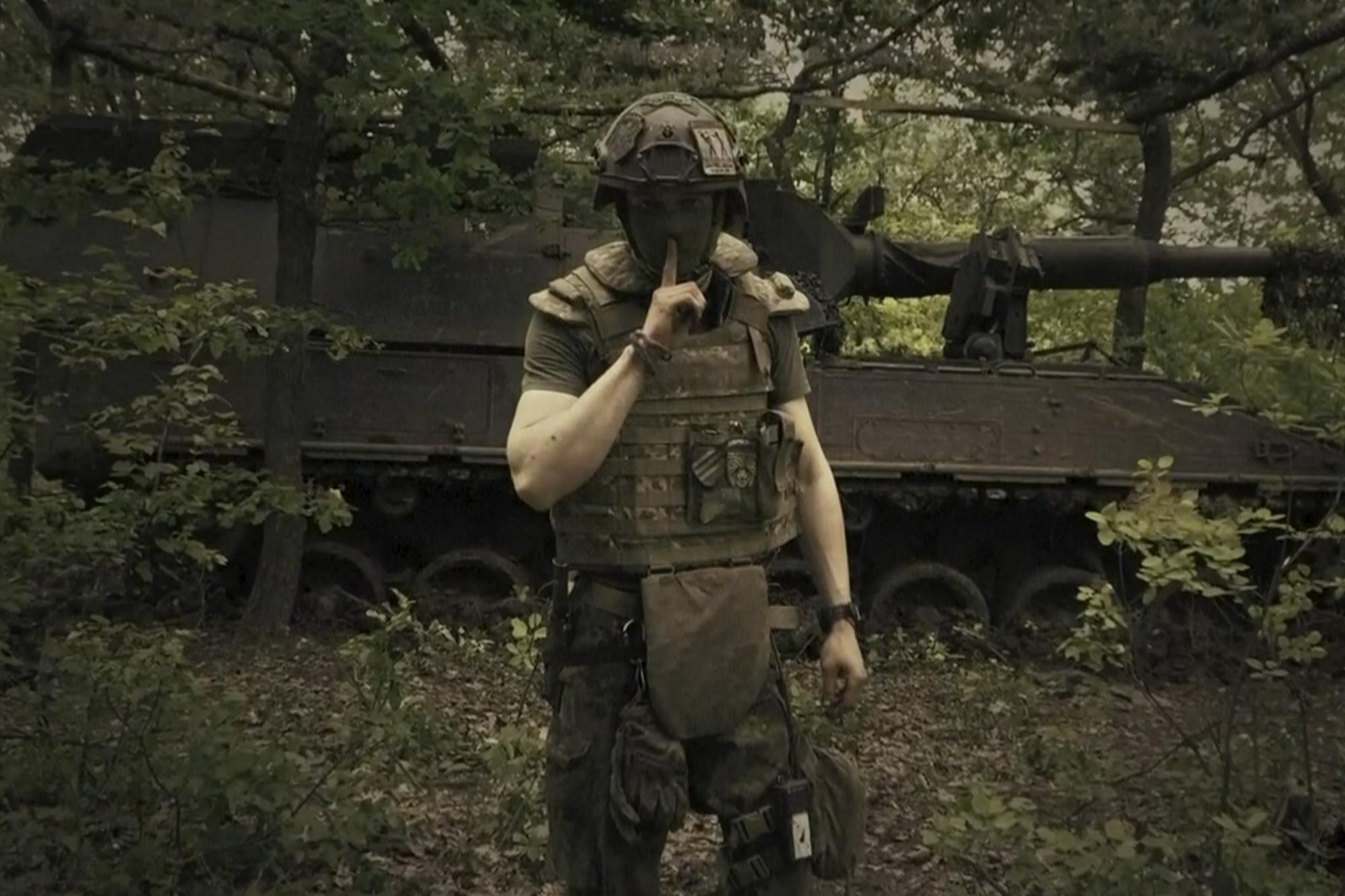 In this image made from video provided by Ukrainian Defense Ministry on Sunday, June 4, 2023, a Ukrainian soldier poses for the camera with his fingers to his lips, in an undisclosed location in Ukraine. A video released by the Ukrainian Defense Ministry on Sunday shows its military gesturing to silence suggesting that no formal announcement of a possible counter offensive against Russia will be made. The on-screen text of the video reads "Plans love silence. There will be no announcement of the start." (Ukrainian Defense Ministry via AP)