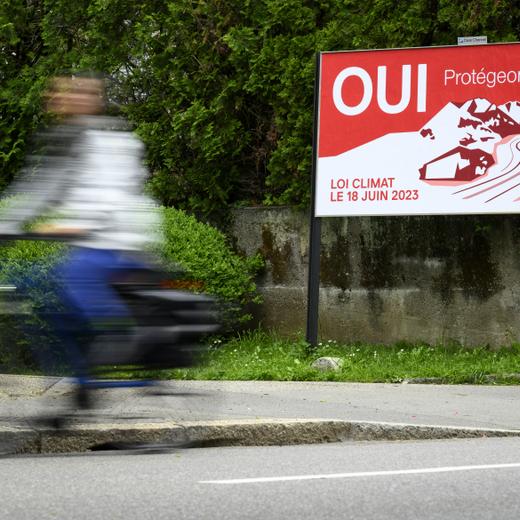 Un velo passe devant une affiche du Parti Socialiste, PS, invitant a voter oui pour la loi sur le climat ce mardi 16 mai 2023 a Lausanne. Le 18 juin prochain la population suisse va se prononcer lors d'une votation populaire sur la loi federale sur les objectifs en matiere de protection du climat, sur l'innovation et sur le renforcement de la securite energtique (LCI). (KEYSTONE/Laurent Gillieron)