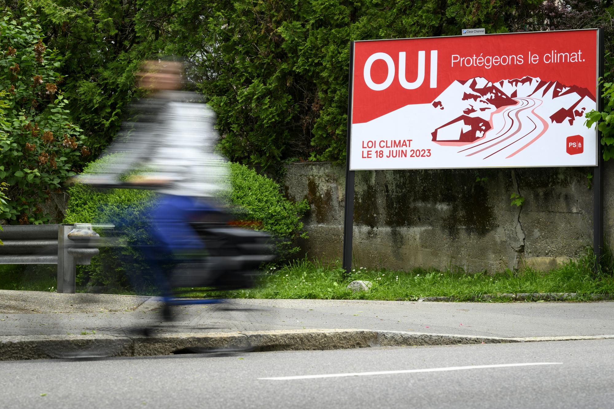 Un velo passe devant une affiche du Parti Socialiste, PS, invitant a voter oui pour la loi sur le climat ce mardi 16 mai 2023 a Lausanne. Le 18 juin prochain la population suisse va se prononcer lors d'une votation populaire sur la loi federale sur les objectifs en matiere de protection du climat, sur l'innovation et sur le renforcement de la securite energtique (LCI). (KEYSTONE/Laurent Gillieron)