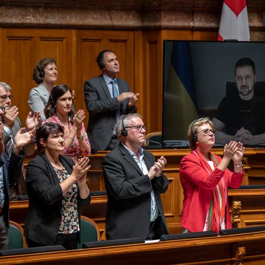 Swiss MPs applaud at the end of a video address of Ukraine's President Volodymyr Zelensky (on screen) during a session at the Swiss parliament in Bern on June 15, 2023. (Photo by Fabrice COFFRINI / AFP)