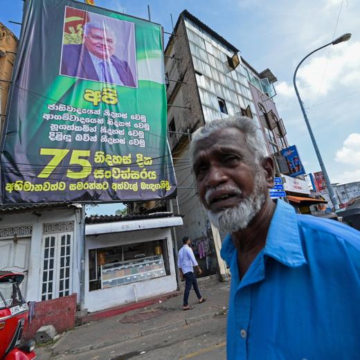Commuters walk past a cut-out banner of Sri Lanka's President Ranil Wickremesinghe, installed along a street in Colombo on March 22, 2023. Wickremesinghe told the national parliament that the International Monetary Fund approving Sri Lanka's rescue program on March 20 was only the beginning of more difficult structural reforms. (Photo by Ishara S. KODIKARA / AFP)