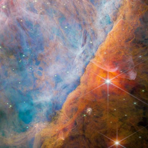 An international team of scientists have used data collected by the NASA/ESA/CSA James Webb Space Telescope to detect a molecule known as the methyl cation (CH3+) for the first time, located in the protoplanetary disc surrounding a young star. They accomplished this feat with a cross-disciplinary expert analysis, including key input from laboratory spectroscopists. The vital role of CH3+ in interstellar carbon chemistry has been predicted since the 1970s, but Webb's unique capabilities have finally made observing it possible — in a region of space where planets capable of accommodating life could eventually form. This image is NIRCam's view of the Orion Bar region studied by the team of astronomers. Bathed in harsh ultraviolet light from the stars of the Trapezium Cluster, it is an area of intense activity, with star formation and active astrochemistry. This made it a perfect place to study the exact impact that ultraviolet radiation has on the molecular makeup of the discs of gas and dust that surround new stars. The radiation erodes the nebula's gas and dust in a process known as photoevaporation; this creates the rich tapestry of cavities and filaments that fill the view. The radiation also ionises the molecules, causing them to emit light — not only does this create a beautiful vista, it also allows astronomers to study the molecules using the spectrum of their emitted light obtained with Webb's MIRI and NIRSpec instruments. The two very large, bright stars are two of the three stars in the θ² Orionis system — the Trapezium Cluster is also known as θ¹ Orionis. The brightest star here, θ² Orionis A, is surrounded by particularly bright and red puffs of dust, which are reflecting the star's light towards Earth. Its great brightness — it is visible with the naked eye — is due to the fact that θ² Orionis A is itself a ternary system made of three closely bound bright stars. There are more proplyds visible in this image than just d203-506 — the Orion Nebula is replete with such new stars. In the very top left, a tiny star is visible within a long, dusty cocoon. This globule has formed from the star's protoplanetary disc, as the disc is broken down by the energetic radiation of the Trapezium Cluster. Around the globule, a round shockwave is strikingly visible moving through the gas of the Orion Nebula. [Image description: A nebula made of many layers of cloudy, colourful material. The top-left side of the image is brightly lit, filled with wispy, thin material in pale shades of pink and blue. A thick bar of denser, cloudier material crosses diagonally at the bottom right. It begins as orange and grows darker and sparser down to the corner. Two very bright stars, with very long diffraction spikes, lie in this sparse area.]