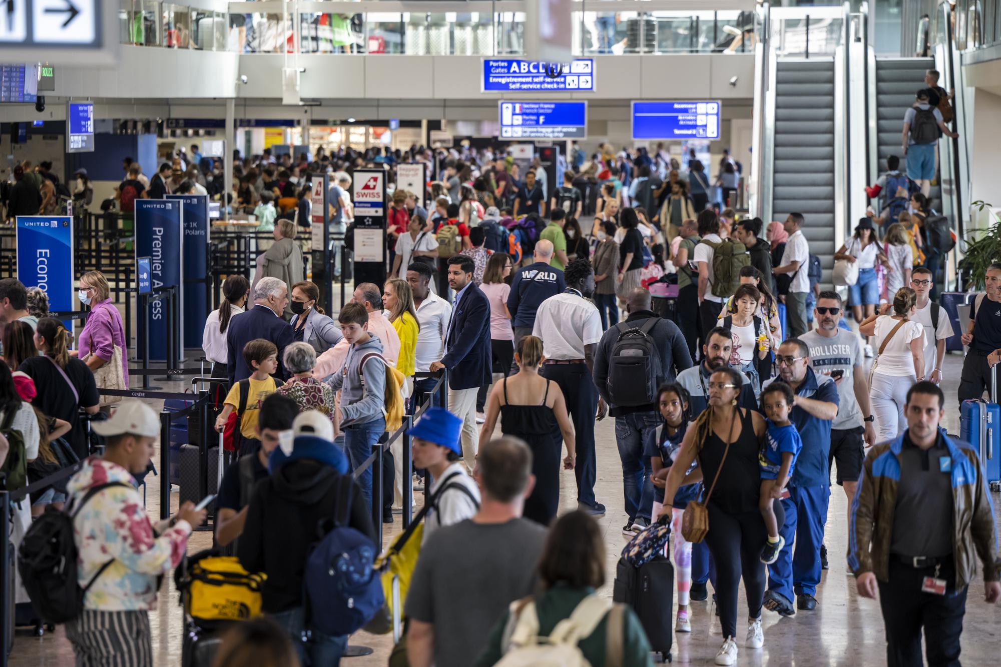 Des passagers attendent avec leurs bagages devant les guichets d'embarquement du terminal principal de l'aeroport international de Geneve, ce samedi 9 juillet 2022 a Geneve. L'aeroport fait face a un fort trafic local de departs de vacances d?ete, une affluence d?environ 100,000 passagers sont attendus ce week-end. (KEYSTONE/Martial Trezzini)