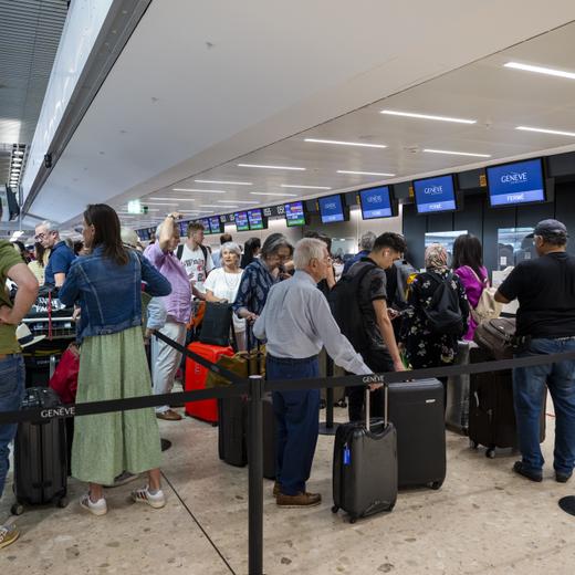 Des passagers attendent avec leurs bagages devant les guichets d'embarquement du terminal principal de l'aeroport international de Geneve, tandis que le syndicat et des employes de l'aeroport de Geneve (AIG) qui manifestent a l'exterieur contre la situation a l'aeroport de Geneve et la nouvelle politique de remuneration de la direction de l'Aeroport qui veut couper dans les salaires du personnel, ce jeudi 29 juin 2023 a Geneve. (KEYSTONE/Martial Trezzini)