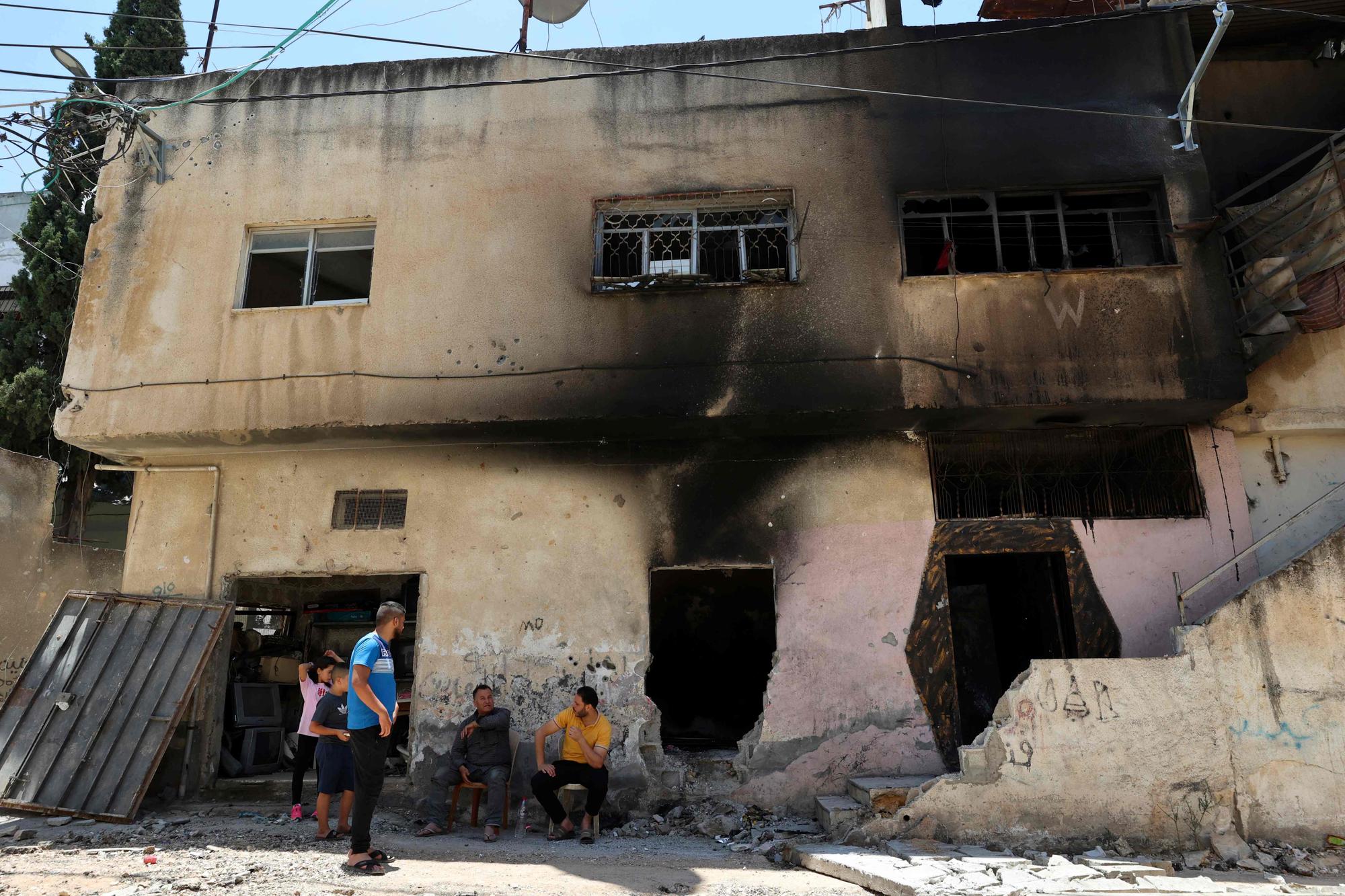 People sit in front of a damaged building in the occupied West Bank Jenin refugee camp on July 6, 2023, following a large-scale Israeli military operation that lasted for two days. The Israeli military launched the raid on the Jenin refugee camp early on July 3, during which 12 Palestinians and one Israeli soldier were killed. (Photo by Zain JAAFAR / AFP)