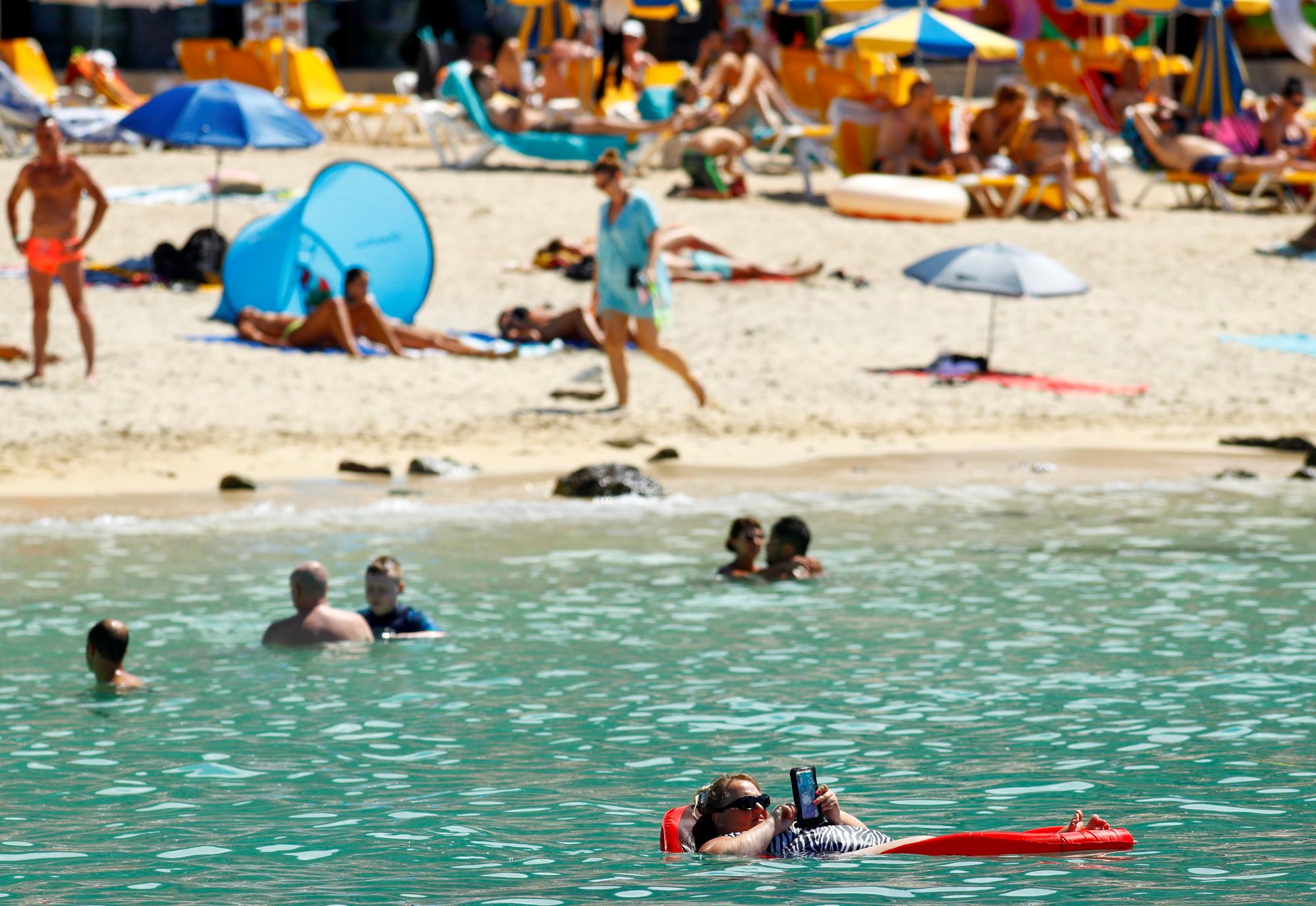 A tourist sunbathes on an air mattress with her phone on the Amadores beach, amid the outbreak of the coronavirus disease (COVID-19) in the south of the island of Gran Canaria, Spain, August 3, 2021. REUTERS/Borja Suarez
