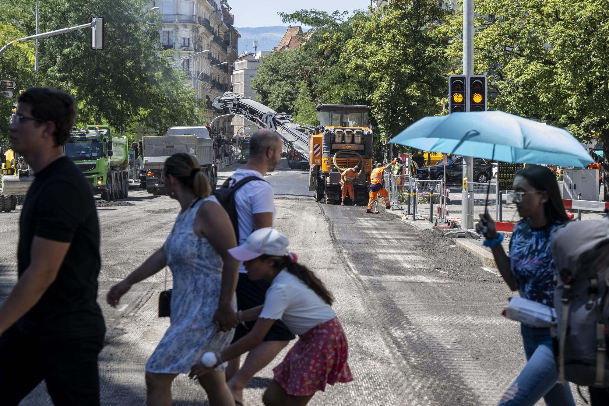 Une personne marche a l?abris de son parapluie afin de se proteger de la chaleur en cette periode de canicule devant des ouvriers qui nettoient la route afin de pouvoir poser un nouveau revetement, un enrobe bitumineux de goudron phonoabsorbant, lors d?une conference de presse du syndicat UNIA afin de denoncer que sur les chantiers publics de genie civil, les conditions legales de protection des travailleurs ne sont pas reunies et mettent en danger leur sante, en periode de canicule. Une bonne soixantaine de chantiers a ete visitee par Unia et une trentaine de denonciations ont ete faites aupres des inspections du travail. Elles concernaient notamment l?absence de pauses regulieres, de mise a disposition d?eau et d?un lieu de pause au frais, ou encore la pratique de travaux lourds aux heures tres chaudes. (KEYSTONE/Martial Trezzini)