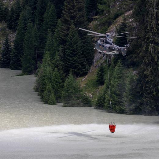 A Swiss Air Force Super Puma helicopter takes water from the Stausee Gibidum to fight a wildfire on the flank of a mountain in Bitsch near Brig, Switzerland, July 18, 2023. REUTERS/Denis Balibouse