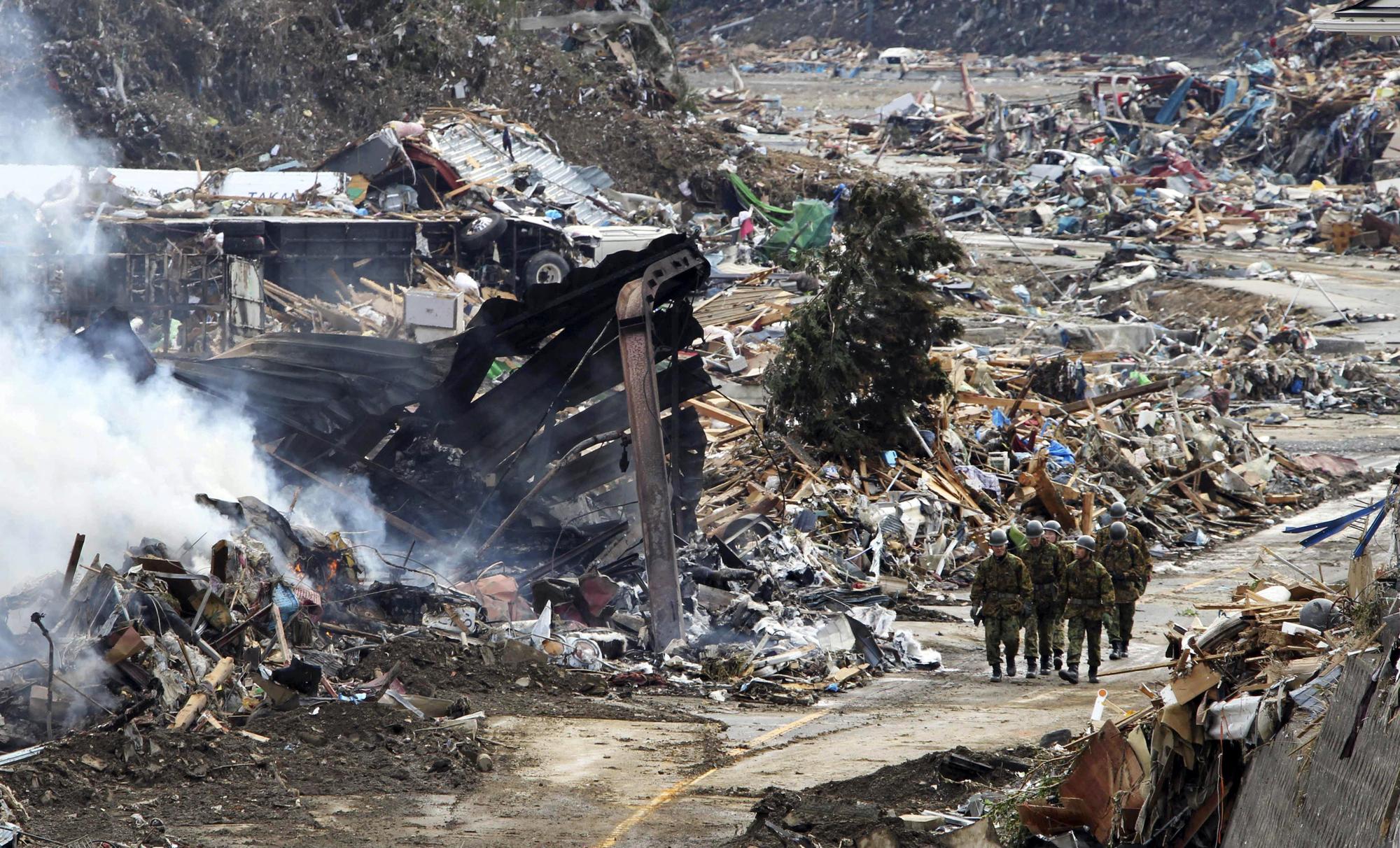 Soldiers walk on debris scattered across the town of Minamisanriku in Miyagi prefecture on March 12, 2011 a day after a massive 8.9 magnitude quake and tsunami hit the region. An explosion at a Japanese nuclear plant triggered fears of a meltdown on March 12, after the massive earthquake and tsunami left more than 1,000 dead and at least 10,000 unaccounted for. JAPAN OUT RESTRICTED TO EDITORIAL USE AFP PHOTO /YOMIURI SHIMBUN (Photo by YOMIURI SHIMBUN / YOMIURI SHIMBUN / AFP)