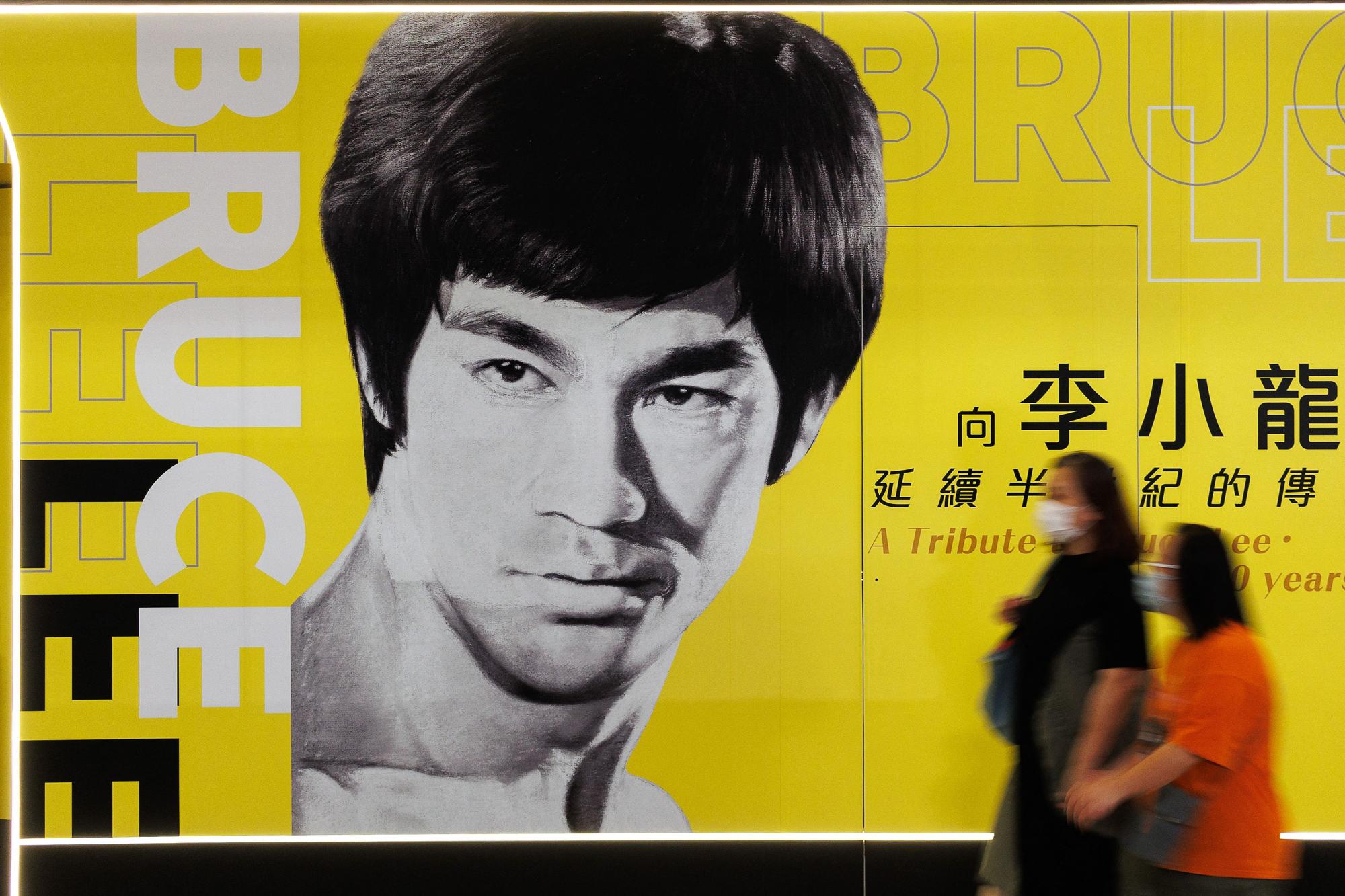 In this photo taken on July 15, 2023 visitors walk past a poster for the Bruce Lee exhibition at the Hong Kong Heritage Museum in Hong Kong, ahead of the 50th anniversary of the martial arts star's death on July 20. The martial arts legend Bruce Lee, whose films spawned a kung fu craze around the world, was one of the first Asian men to achieve Hollywood superstardom, and his influence can still be felt in Hong Kong as fans held exhibitions and martial arts workshops this week to mark the 50th anniversary of his death. (Photo by May JAMES / AFP) / To go with 'HongKong-China-US-entertainment-culture-BruceLee,FEATURE'