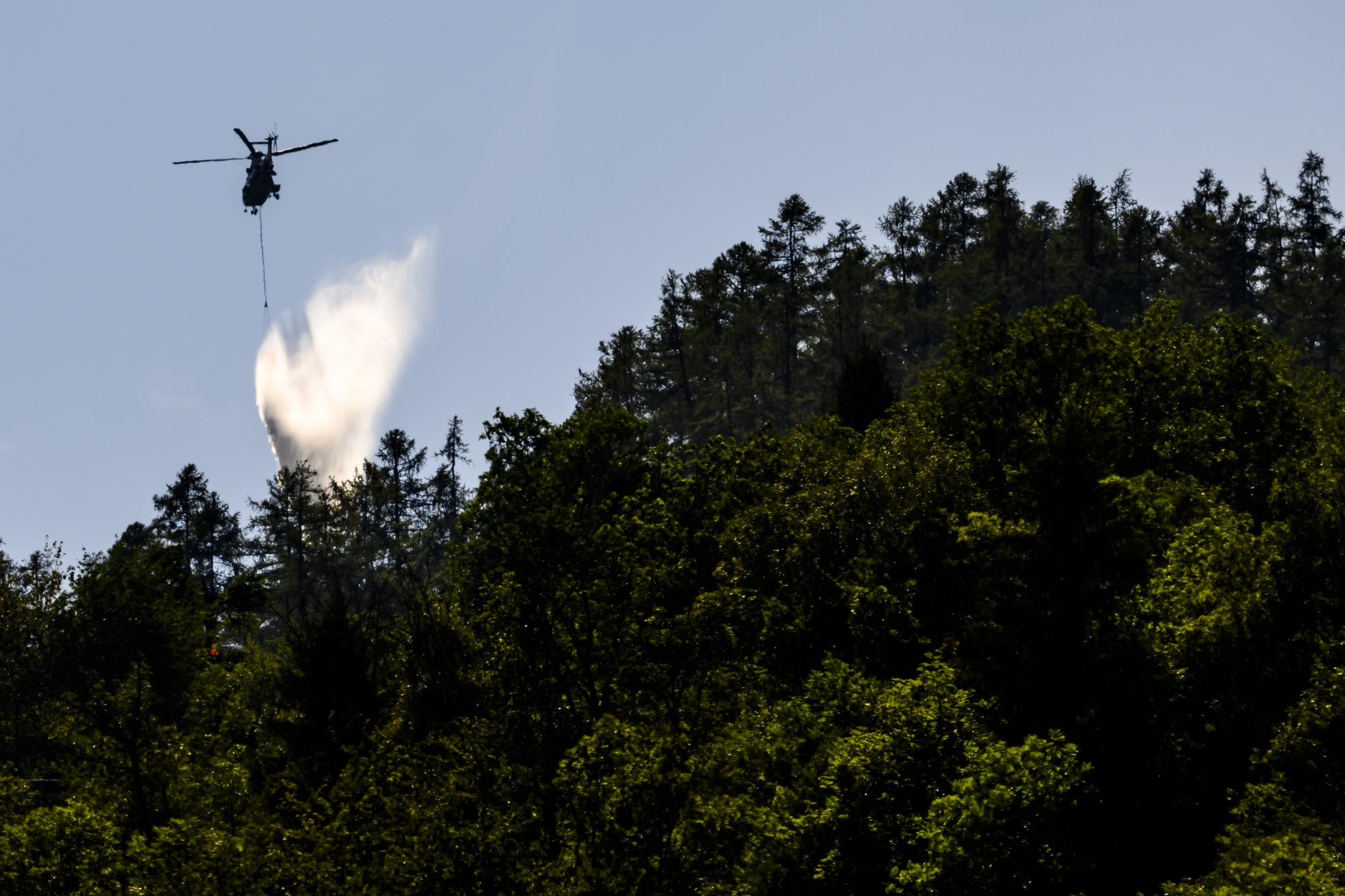Un helicoptere Super Puma de l'armee, verse de l'eau pour eteindre les foyers dans la foret au-dessus des communes de Bitsch et Ried-Moerel le jeudi 20 juillet 2023 depuis Moerel Filet. Six helicopteres, dont un Super Puma de l'armee, ont repris du service. Ils travaillent dans des zones ou il n'y a pas de pompiers au sol. (KEYSTONE/Jean-Christophe Bott)