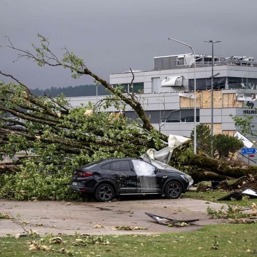 A picture taken on July 24, 2023 shows a damaged car next to an uprooted tree, a few hours after a violent storm hit the aera in Le Cret-du-Locle near La Chaux-de-Fonds, western Switzerland. According to local media, at least one person was killed, when a crane fell. (Photo by Fabrice COFFRINI / AFP)