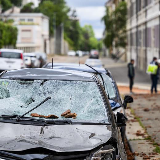 Une personne marche entre les voitures endommagees par la chute des tuiles d'un toit, un jour apres la forte tempete le mardi 25 juillet 2023 a La Chaux-de-Fonds. Le deblaiement des materiaux et la reparation des infrastructures ont repris mardi a La Chaux-de-Fonds dans le canton de Neuchatel, apres la violente tempête de la veille. (KEYSTONE/Jean-Christophe Bott)