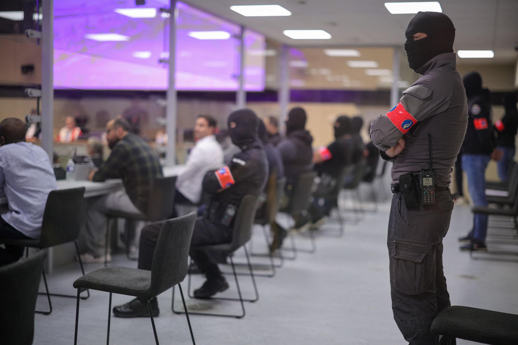 Security personnel oversee defendants as they sit in a specially designed glass box in the courtroom as an unseen judge announces the verdict in the Brussels terrorist attack trial in the Palace of Justice building in Brussels on July 25, 2023. Ten defendants are on trial for the 2016 terrorist attacks on Zaventem airport and Maelbeek metro station which resulted in the deaths of 32 people and left hundreds injured. (Photo by OLIVIER MATTHYS / POOL / AFP)