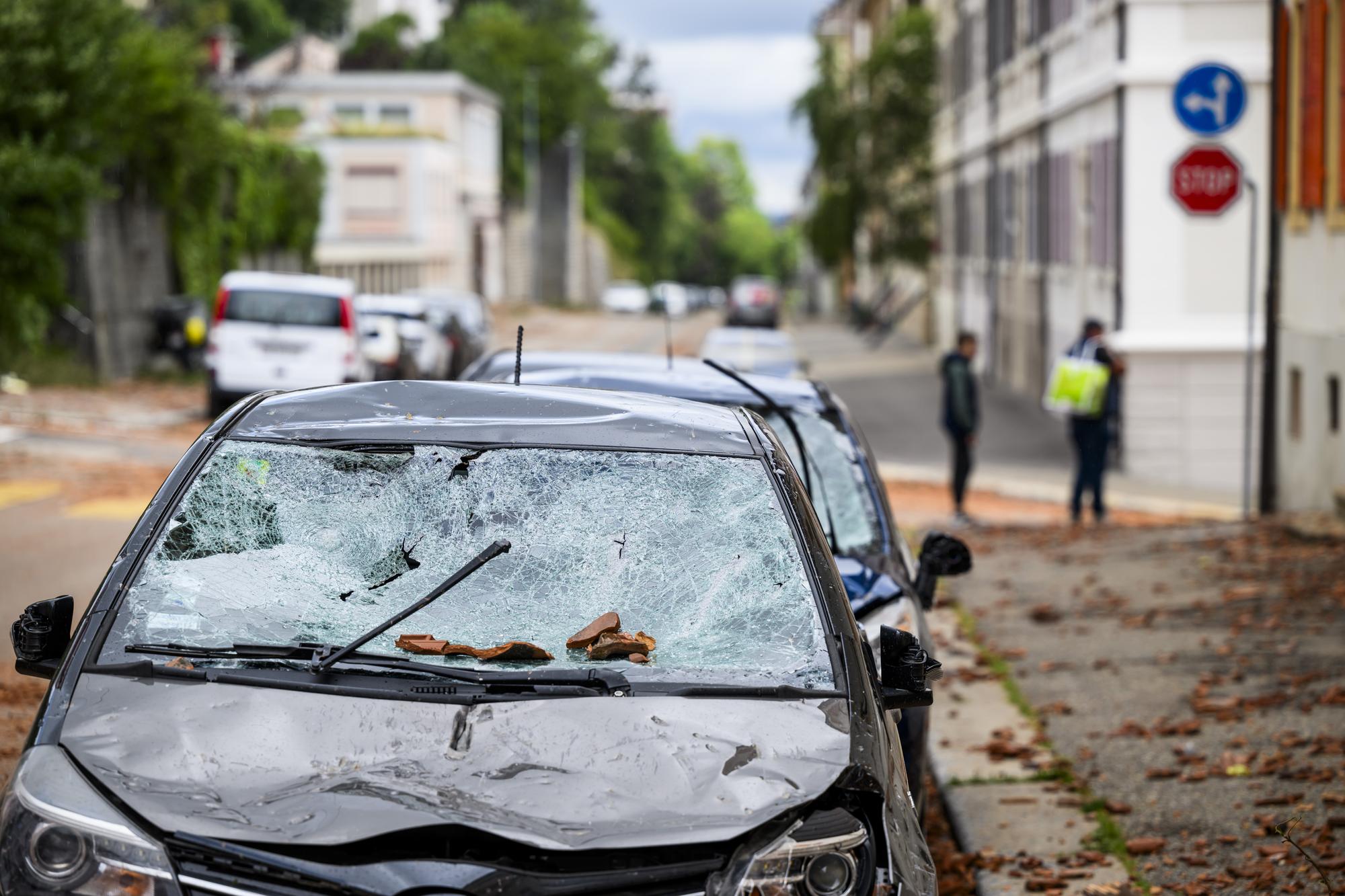 Une personne marche entre les voitures endommagees par la chute des tuiles d'un toit, un jour apres la forte tempete le mardi 25 juillet 2023 a La Chaux-de-Fonds. Le deblaiement des materiaux et la reparation des infrastructures ont repris mardi a La Chaux-de-Fonds dans le canton de Neuchatel, apres la violente tempête de la veille. (KEYSTONE/Jean-Christophe Bott)
