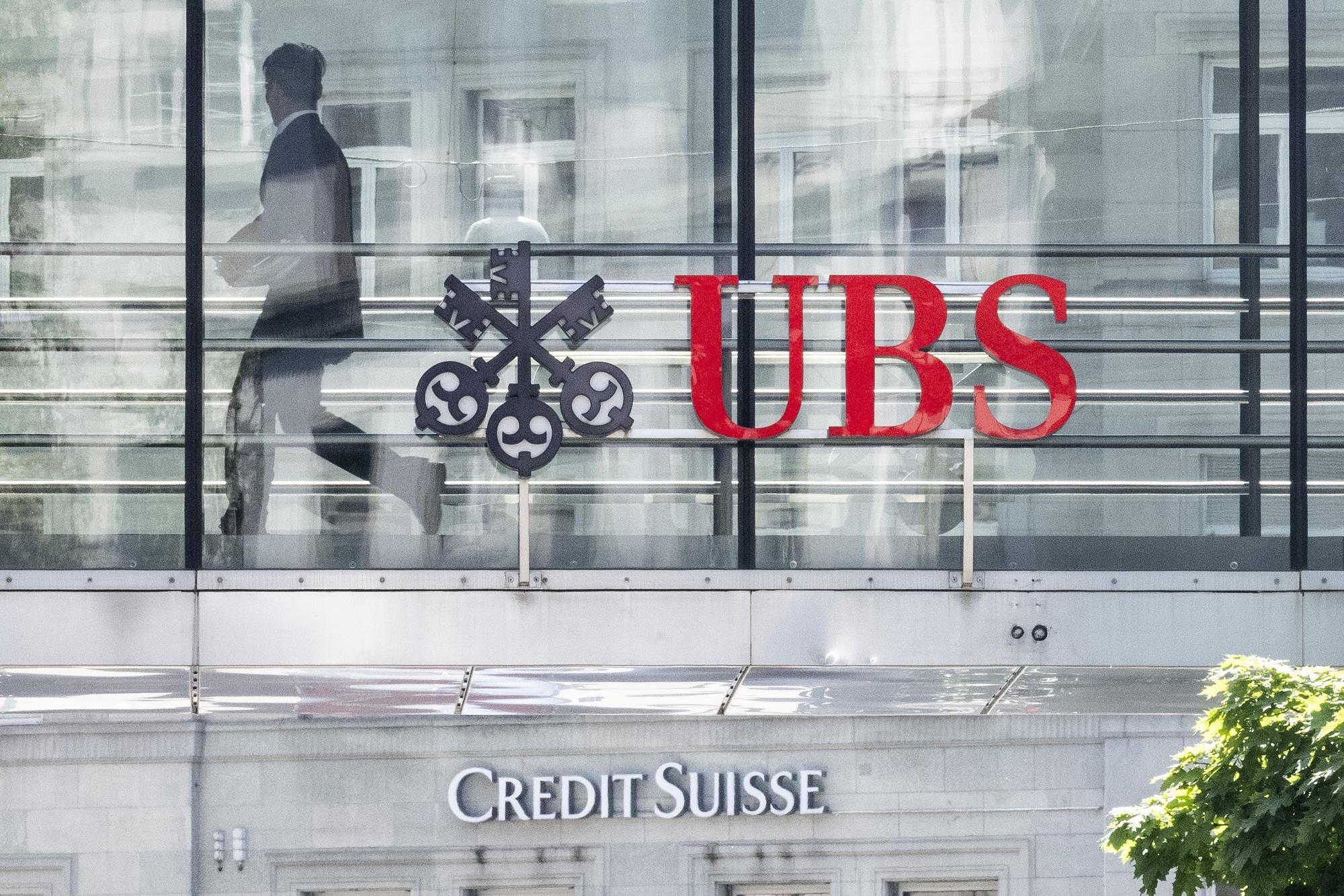 Ein Mann laeuft zwischen den beiden Logos der Banken UBS und Credit Suisse, aufgenommen am Montag, 12. Juni 2023 in Zuerich. Heute verkuendete die nunmehr einzige Schweizer Grossbank in einem offenen Brief: Die Uebernahme der Credit Suisse durch die UBS ist vollzogen. (KEYSTONE/Ennio Leanza)