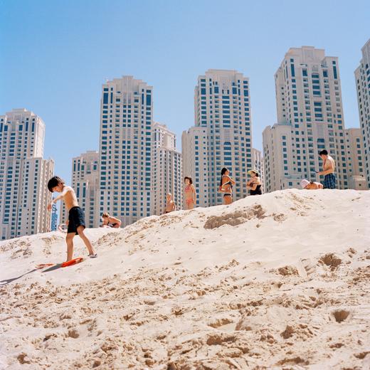 Un enfant avance palmes aux pieds sur la plage de la Jumeirah Beach Residence; Dubaï.  Issue de la série DUBAÏ, LA NON VILLE  "Singapour ? Calcutta ? Le Caire ? Dubaï, cité globale, à la fois arabe et occidentale, est tout cela à la fois. Elle cumule les paradoxes. Elle étale ses gratte-ciels improbables, tendus vers un ciel toujours plus proche, mais aussi ses petites maisons traditionnelles, rectangulaires, tassées. Elle s'enorgueillit de ses grandes artères vides de passants, en négligeant ses souks aux rues étroites et pleines de charme. C'est un gigantesque port industriel sans histoire, une ville ouvrière sans histoire ouvrière. Un empire urbain géant sans banc ni place, avec cafés climatisés et terrasses protégées. Bref, un endroit où personne ne promène son chien… On observe cette autoroute immense de loin, de haut, comme une maquette de construction irréelle. Et on se pince le bras : tout cela existe t'il vraiment ? C'est assurément l'un des endroits les plus étranges sur terre. Mais est-ce vraiment une ville ?" Johanna Luyssen