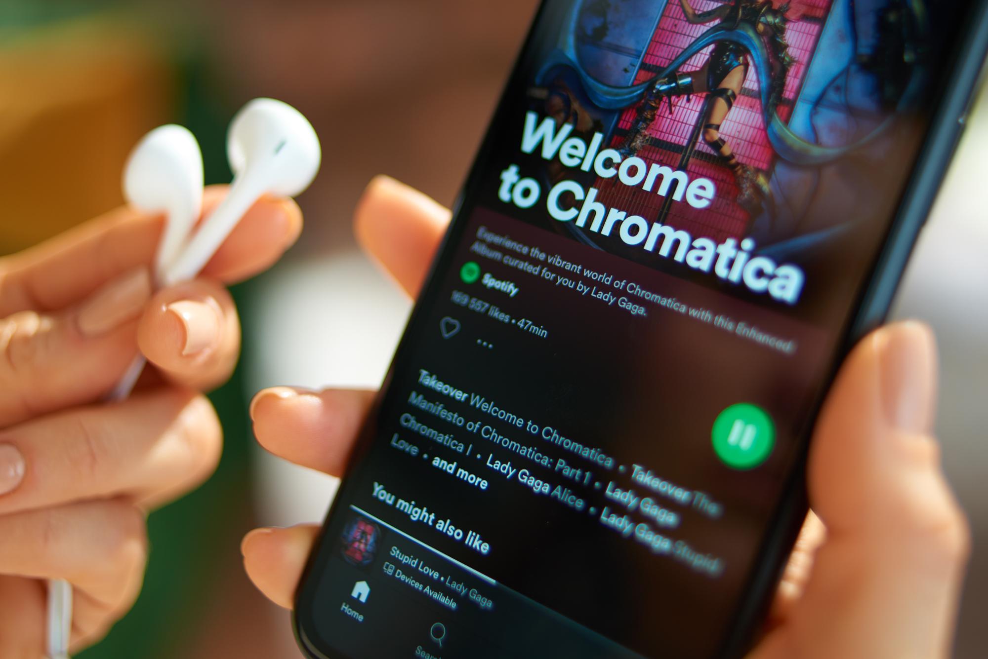 PRAGUE - May, 29, 2020: Closeup on hands of female with white headphones and smartphone with new Lady Gaga album Chromatica playing on Spotify app.