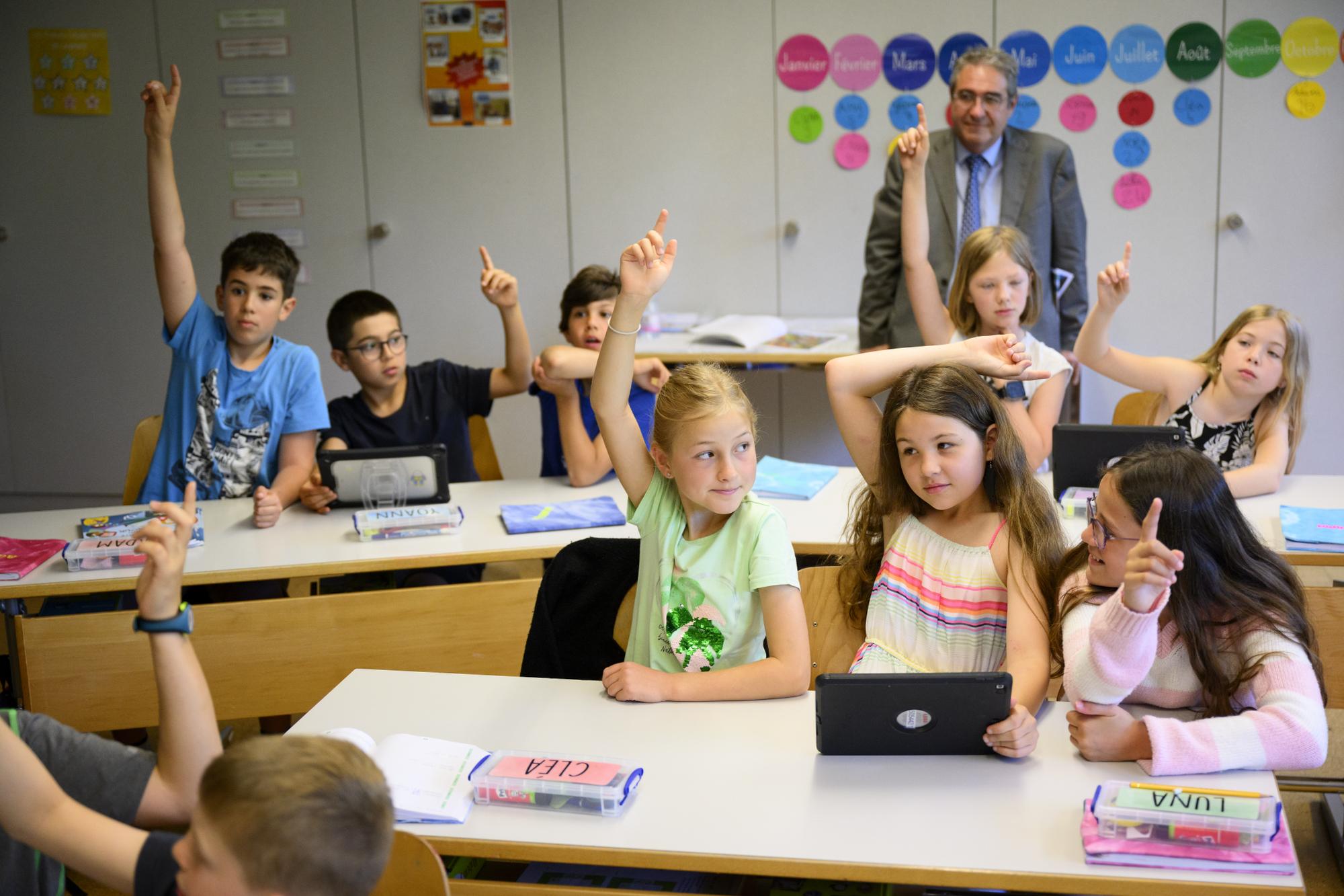 Le conseiller d'Etat vaudois Frederic Borloz, droite, derriere, observe des eleves de 6eme annee primaire, 6P, enfant de 9-10 ans, travaillant a l'aide d'une tablette un cours d'education numerique au sujet des ecrans et des pratiques numeriques ce lundi 12 juin 2023 a l'ecole du college intercommunal de l'Etablissement primaire Villars-le-Terroir - Poliez-Pittet a Poliez-Pittet dans le canton de Vaud. (KEYSTONE/Laurent Gillieron)