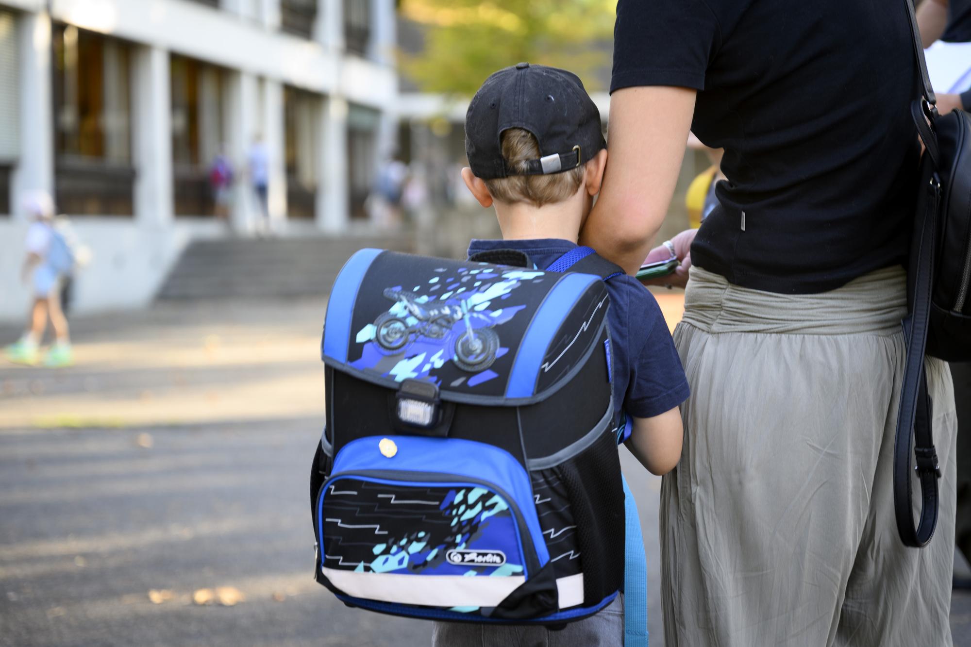 Un eleve arrive dans la court de l'ecole accompagne de sa maman le jour de la rentree scolaire des ecoliers vaudois ce lundi 22 aout 2022 dans l'ecole de l'etablissement primaire de Floreal a Lausanne. (KEYSTONE/Laurent Gillieron)