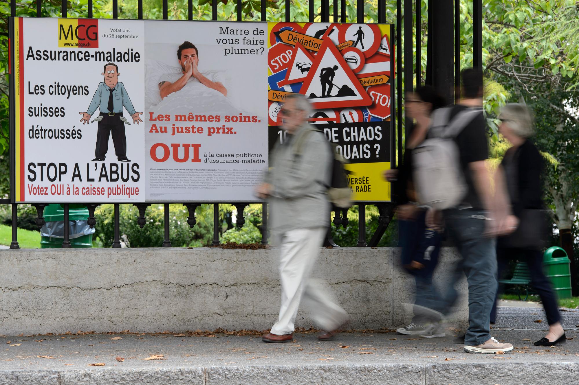 Des personnes passent devant des affiches sur les differents themes des votations federales et cantonales, ce dimanche 30 aout 2014 a Geneve. Les citoyens genevois se prononceront le 28 septembre sur differents objets en votations federales, cantonale, donc la traversee de la Rade, la TVA pour la restauration, et pour l'assurance maladie et la caisse unique. (KEYSTONE/Martial Trezzini)