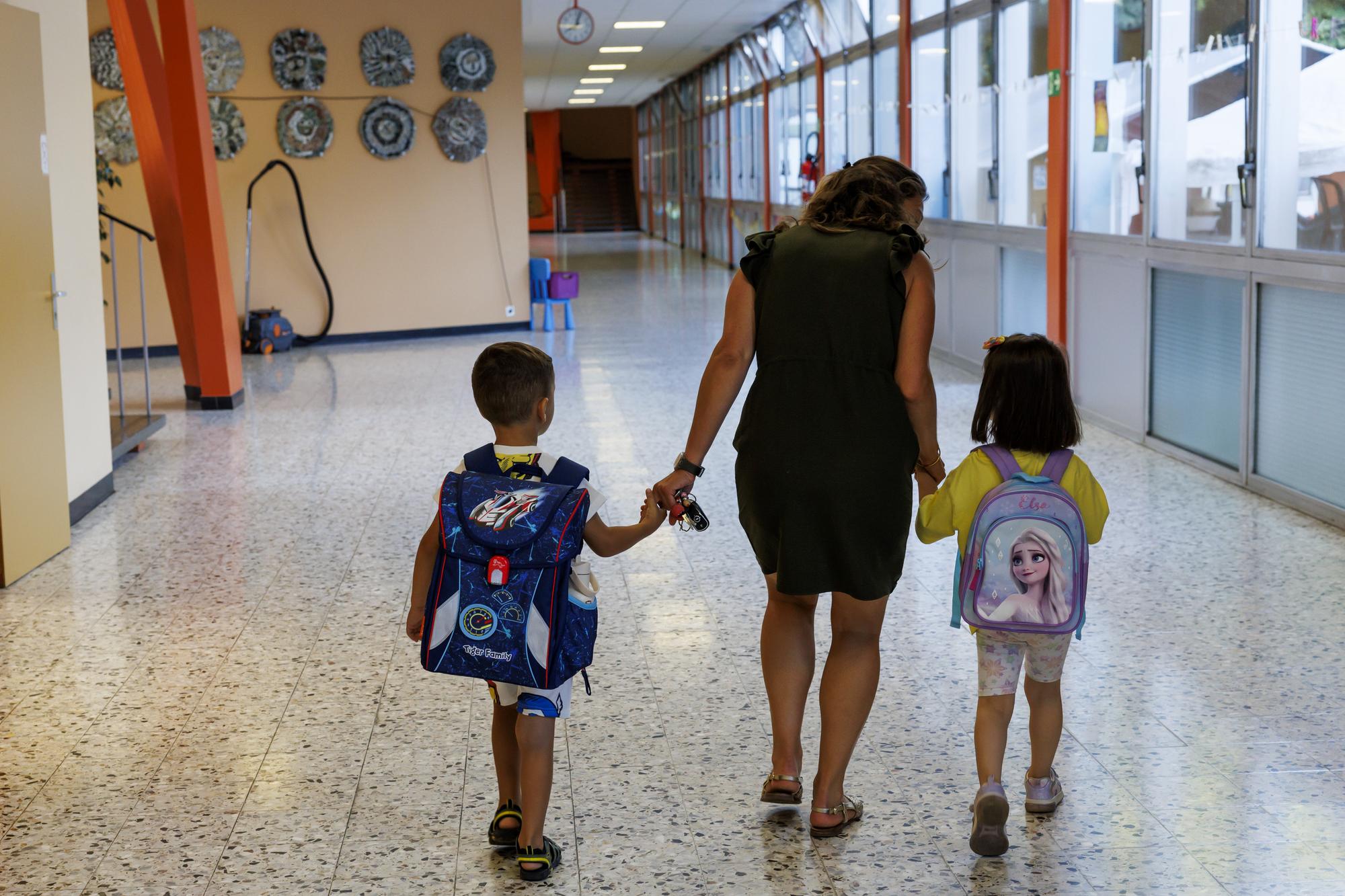 Une maman accompagne ses enfants dans leur classe a l'ecole des Tattes lors de la rentree scolaire 2023-24, ce lundi 21 aout 2023 a Onex pres de Geneve. (KEYSTONE/Salvatore Di Nolfi)