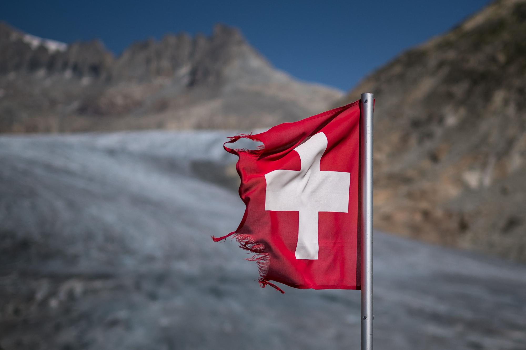 A photograph taken on August 24, 2023 above Gletsch, in the Alps shows a frayed Swiss flag next to the melting Rhone Glacier. A leading Swiss glaciologist warned on August 16, 2023 that 2023 was looking "not good" for the country's glaciers, a year after they suffered a record melt. "Still more than a month to go in the melting season. How are Swiss glaciers doing at the moment? Not good!" glaciology professor Matthias Huss, head of Glacier Monitoring in Switzerland (GLAMOS), said on the platform X, formerly known as Twitter. (Photo by Fabrice COFFRINI / AFP)
