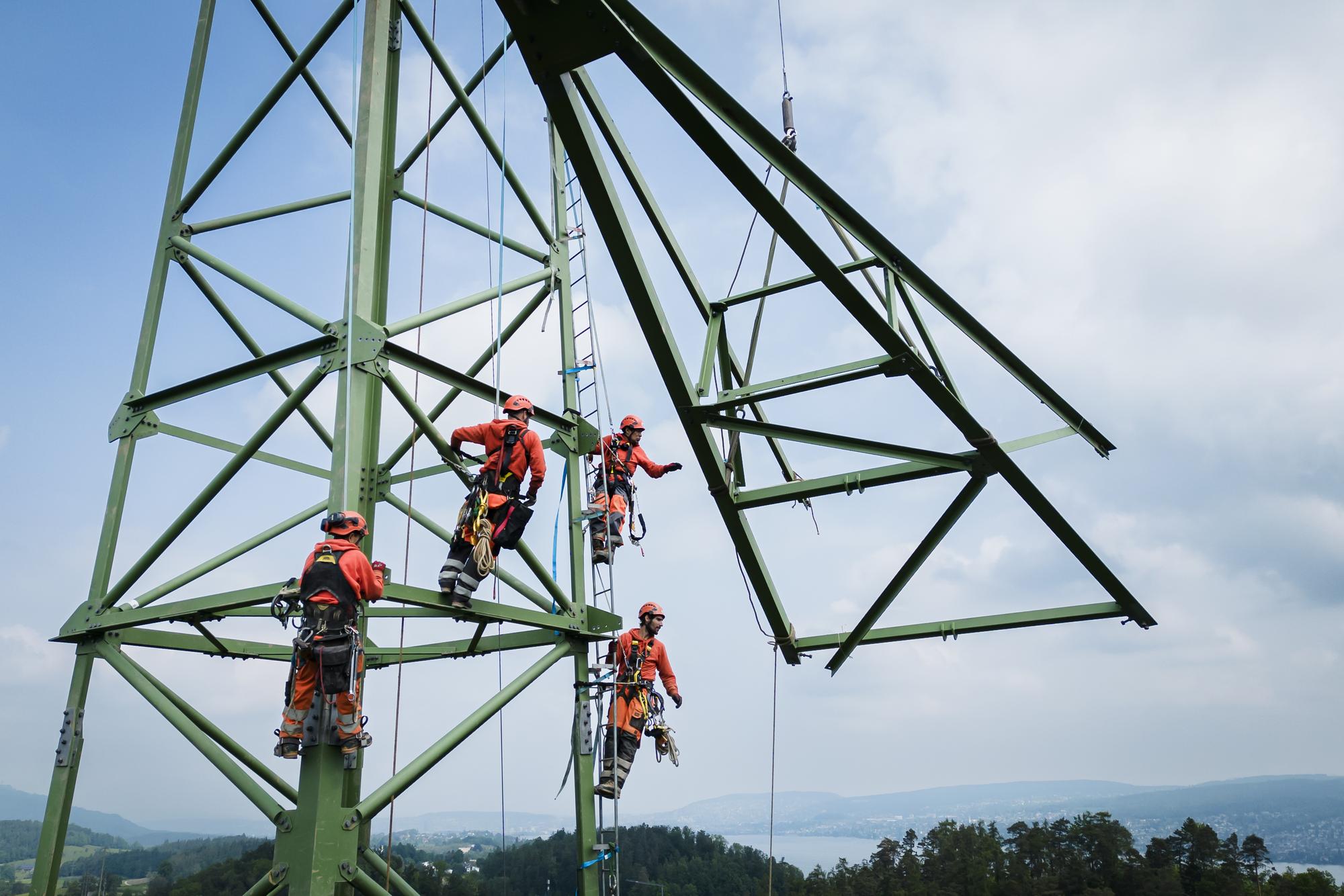 Arbeiter montieren einen Quertraeger an einem Mast einer Hochspannungsleitung der Swissgrid, am Dienstag, 23. Mai 2023 in Gattikon bei Thalwil. Mit der Montage von sechs neuen Masten im Raum Gattikon und dem Anschluss der Unterwerke Thalwil und Waldegg an das Hoechstspannungsnetz und der Verstaerkung der Leitungen zwischen Obfelden und Samstagern wird das Hoechstspannungsnetz auch von Sueden her bis in die Stadt Zuerich herangefuehrt. Dies soll die Transportkapazitaet und Versorgungssicherheit der Stadt und Region Zuerich erhoehen. (KEYSTONE/Michael Buholzer)