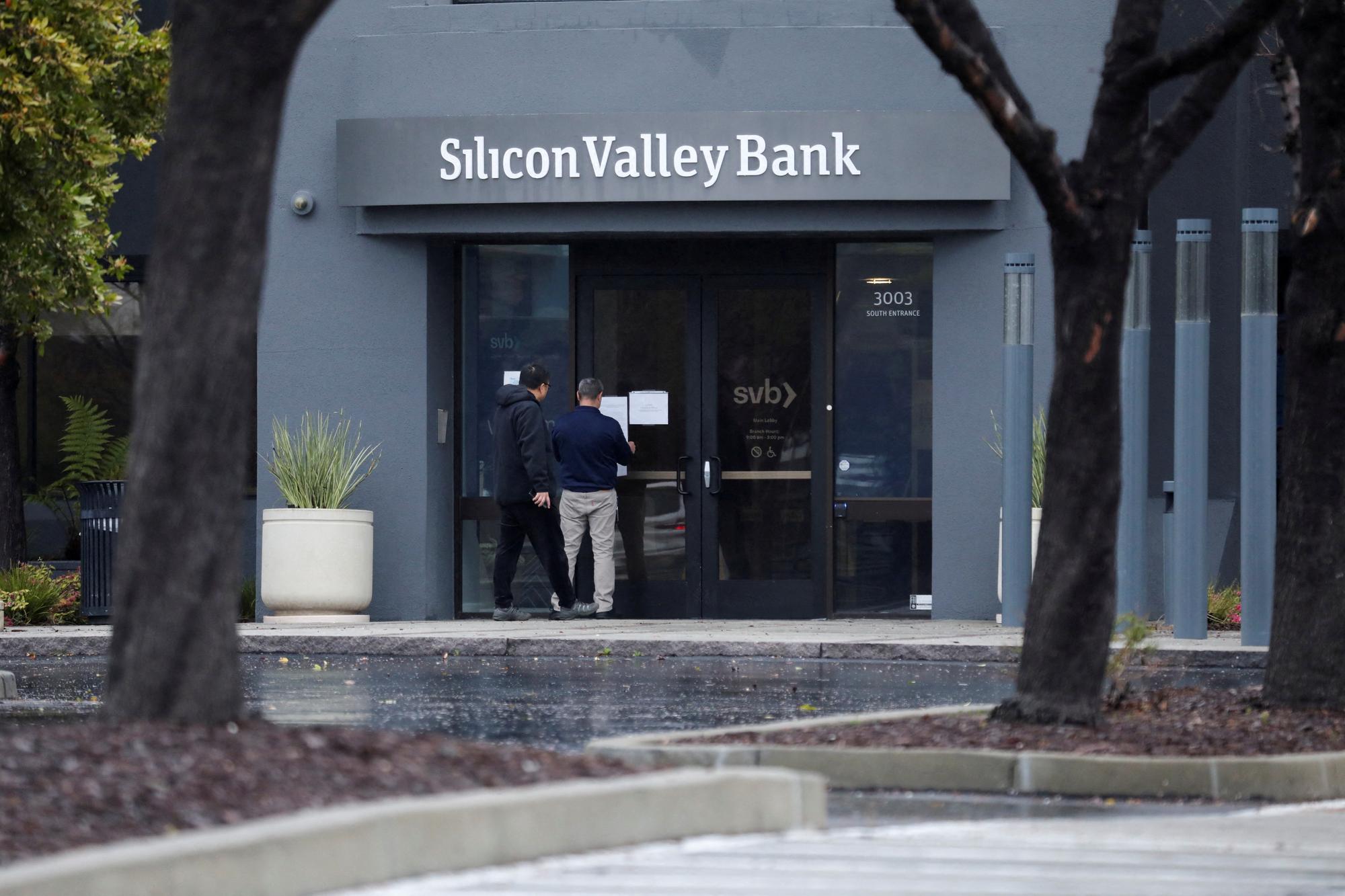FILE PHOTO: A man puts a sign on the door of the Silicon Valley Bank as an onlooker watches at the bank's headquarters in Santa Clara, California, U.S. March 10, 2023. REUTERS/Nathan Frandino/File Photo