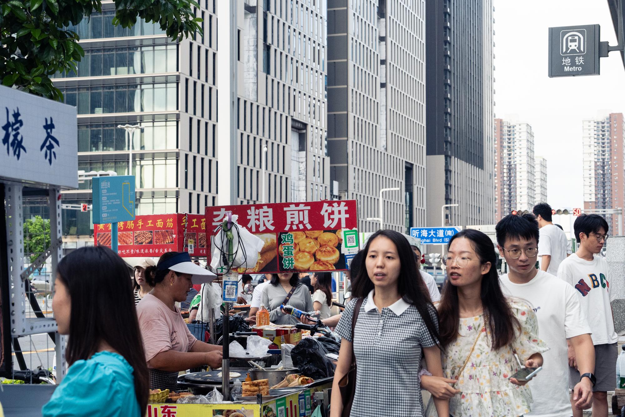 3. September, 2023, Qianhai Bay, Shenzhen. On weekends, this area is crowded with street vendors and tourists, behind them, several skyscrapers under construction lined up along the street. Qianhai was considered a new business district with a promising future, planned as the Qianhai Shenzhen-Hong Kong Modern Service Industry Cooperation Zone, with special measures to encourage Hong Kong companies to set up branches on the mainland. However, during the pandemic, vacant office space became a significant problem, with the vacancy rate as high as 24.9% in 2022.
