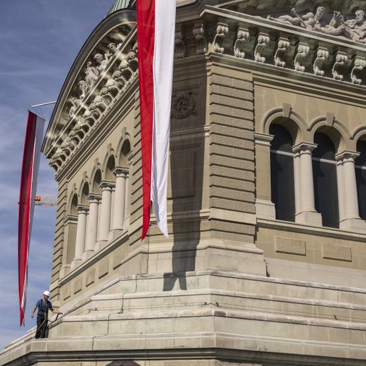Bernhard Egger vom Bundesamt fuer Bauten und Logistik BBL, sichert eine der vier rot-weissen Fahnen, die an den vier Kanten der Hauptkuppel angehaengt sind, auf dem Dach des Parlamentsgebaeudes, am ersten Tag der Herbstsession der Eidgenoessischen Raete, am Montag, 11. September 2023 in Bern. (KEYSTONE/Alessandro della Valle)