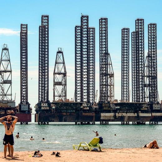 Men rest on a beach on the shore of the Caspian Sea in front of oil rigs following the easing of strict quarantine measures against the spread of the coronavirus disease in Baku on August 5, 2020. (Photo by TOFIK BABAYEV / AFP) (Photo by TOFIK BABAYEV/AFP via Getty Images)