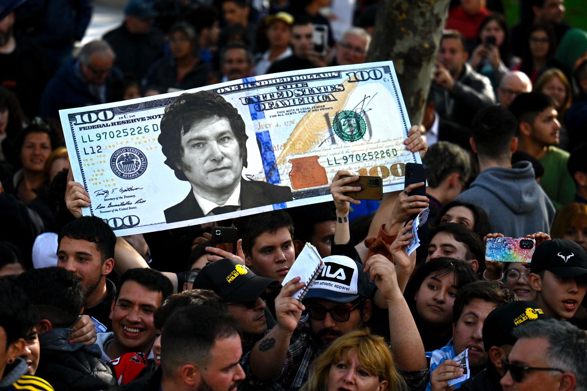 A supporter of Argentine congressman and presidential candidate for the La Libertad Avanza Alliance, Javier Milei, holds a giant 100-dollar bill with his face painted on it during a campaign rally in San Martin, Buenos Aires province, Argentina, on September 25, 2023. (Photo by Luis ROBAYO / AFP)